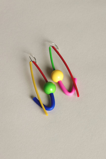 Introducing the Rainbow Sphere Earrings by Samuel Coraux, a striking piece with colorful geometric design. Curved elements in red, pink, blue, and yellow are highlighted by green and yellow beads on a plain background.