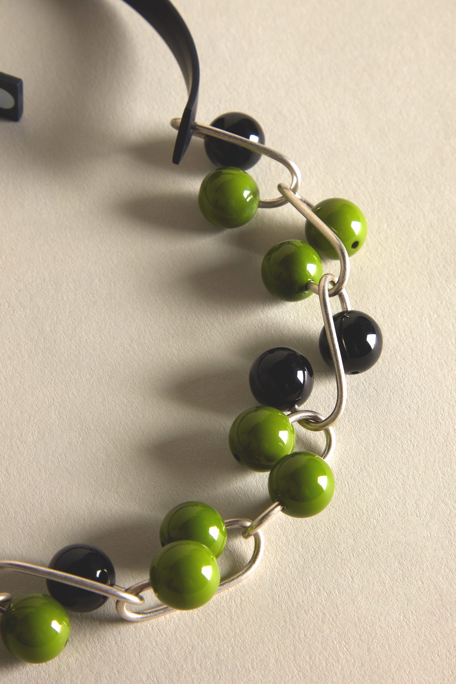 Close-up of a Woven Spheres Necklace by Samuel Coraux, showcasing alternating green and black spherical beads on silver wire in a looped pattern. This sculptural design embodies the artful elegance characteristic of his jewellery collection.