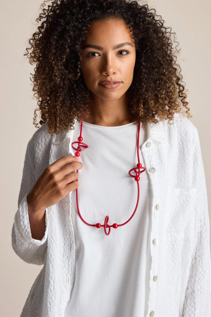 A person with curly hair wearing a white shirt and a bold Trio Squiggle Necklace by Samuel Coraux looks directly at the camera.