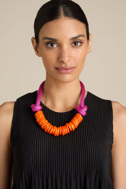 A woman with dark hair wearing a sleeveless black top and a Murano Glass Rings Necklace by Samuel Coraux stands against a beige background.