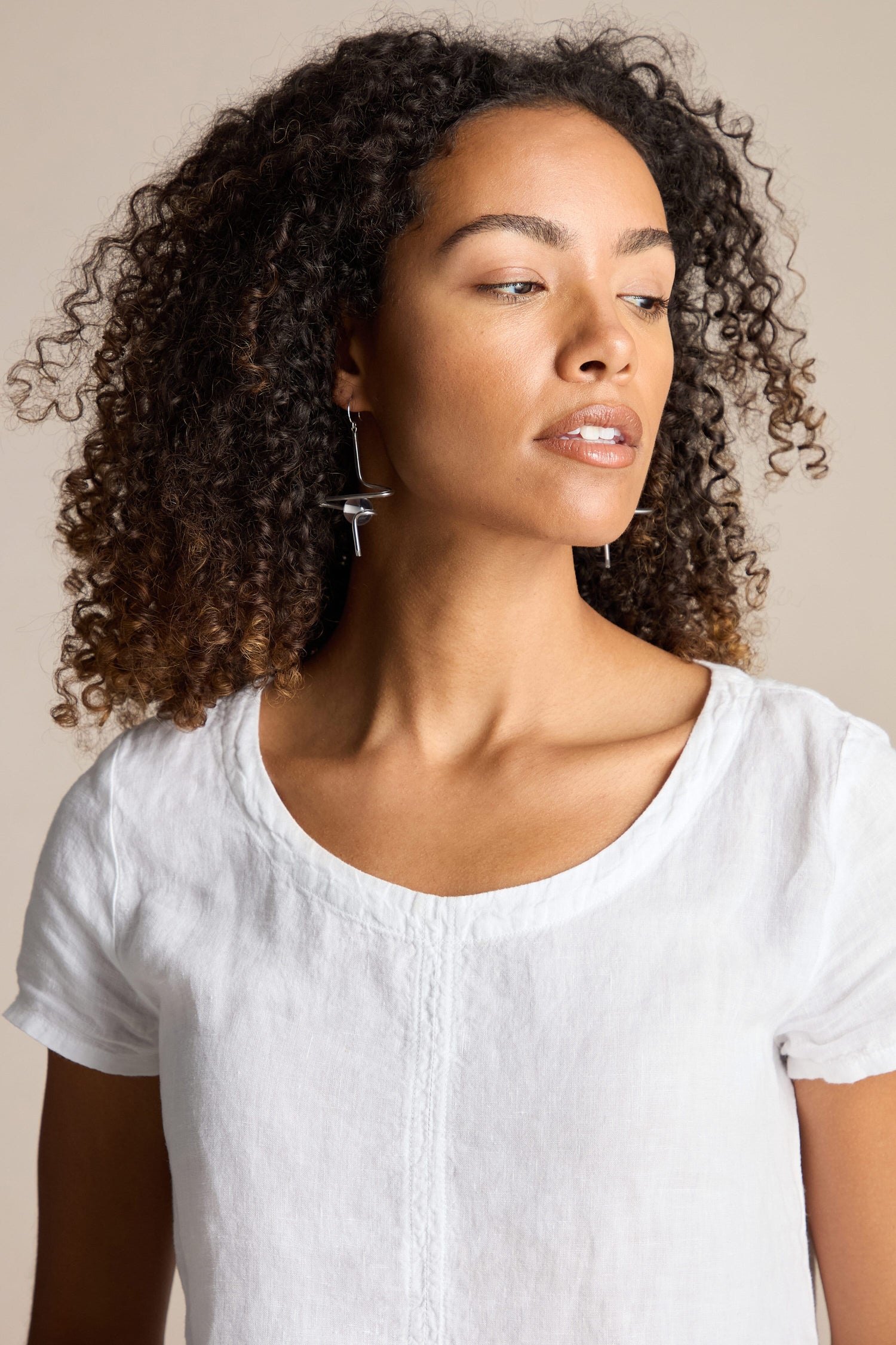 A person with curly hair wearing a white top and Samuel Coraux's Sketch Ball Earrings looks to the side against a neutral background.