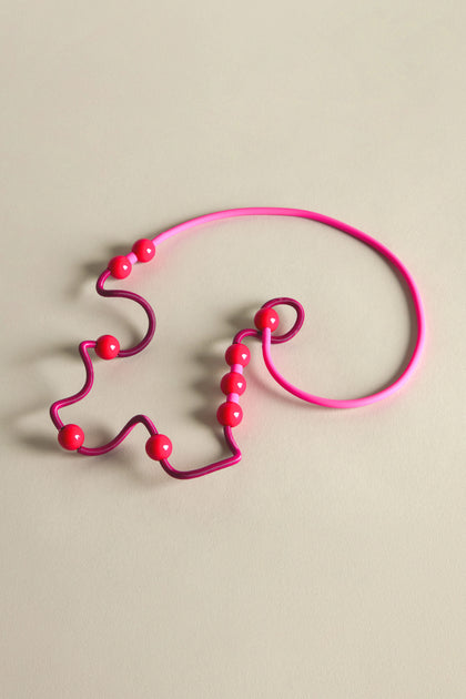 A whimsical French jewelry designer's creation, the Fuchsia Spiral Glass Spheres Necklace is elegantly displayed on a neutral surface, with an eccentric wire design, soft-touch rubber accents, and vibrant pink beads.