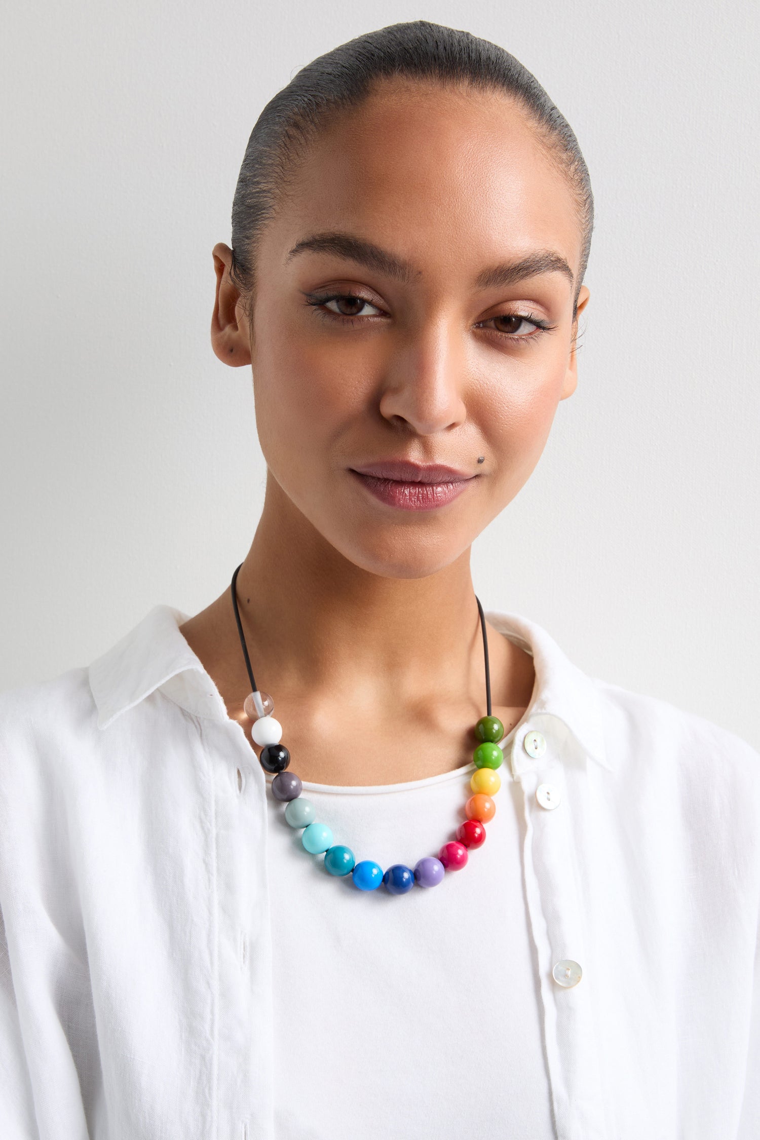 A person in a white shirt poses against a plain background, showcasing the elegance of bold colors with their Smarties Necklace—a piece reminiscent of a French jewelry designer's touch.