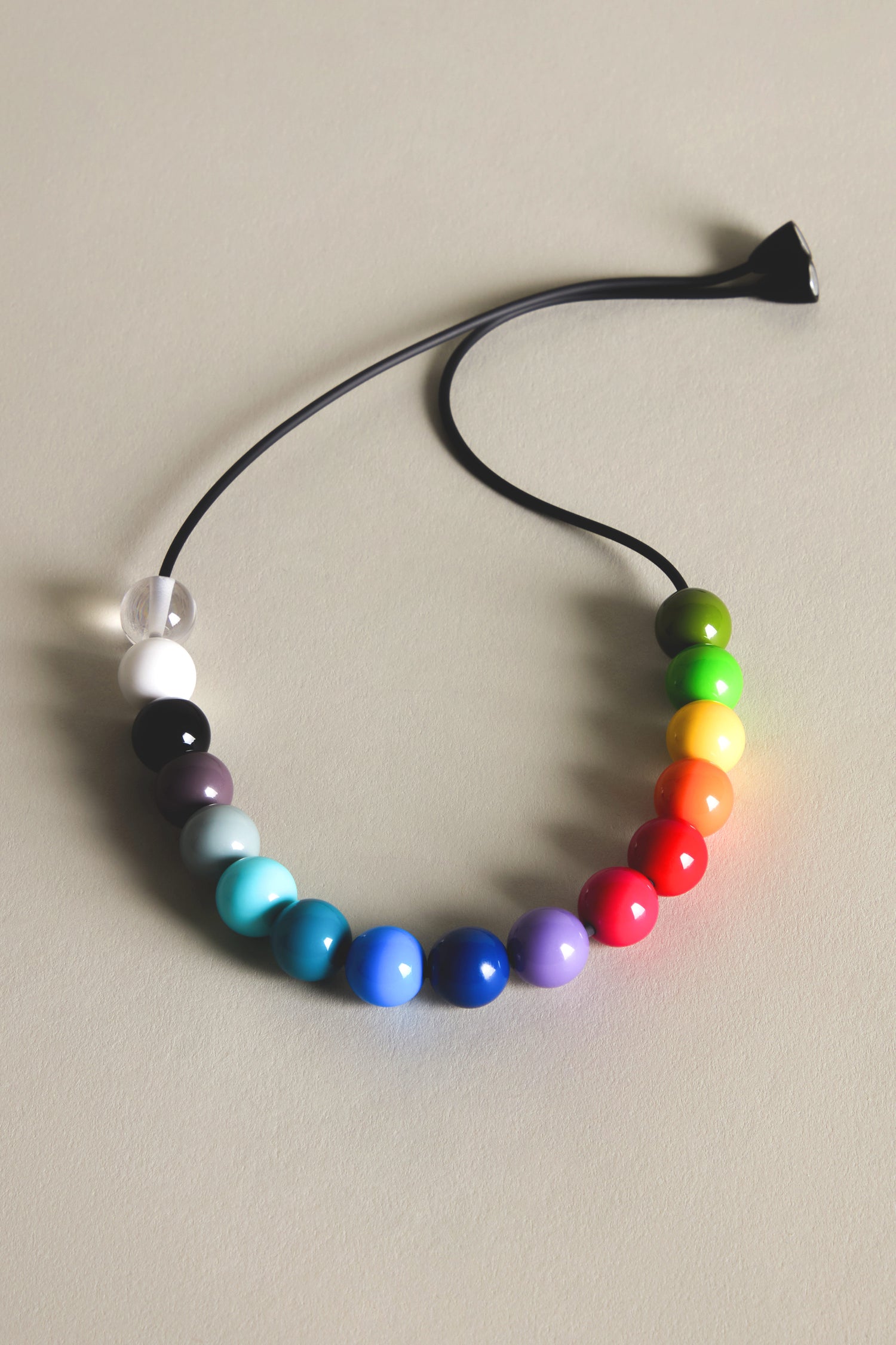 A Smarties Necklace with a cord featuring spherical beads in striking colors transitioning from black to red to green, beautifully arranged on a neutral-toned surface.