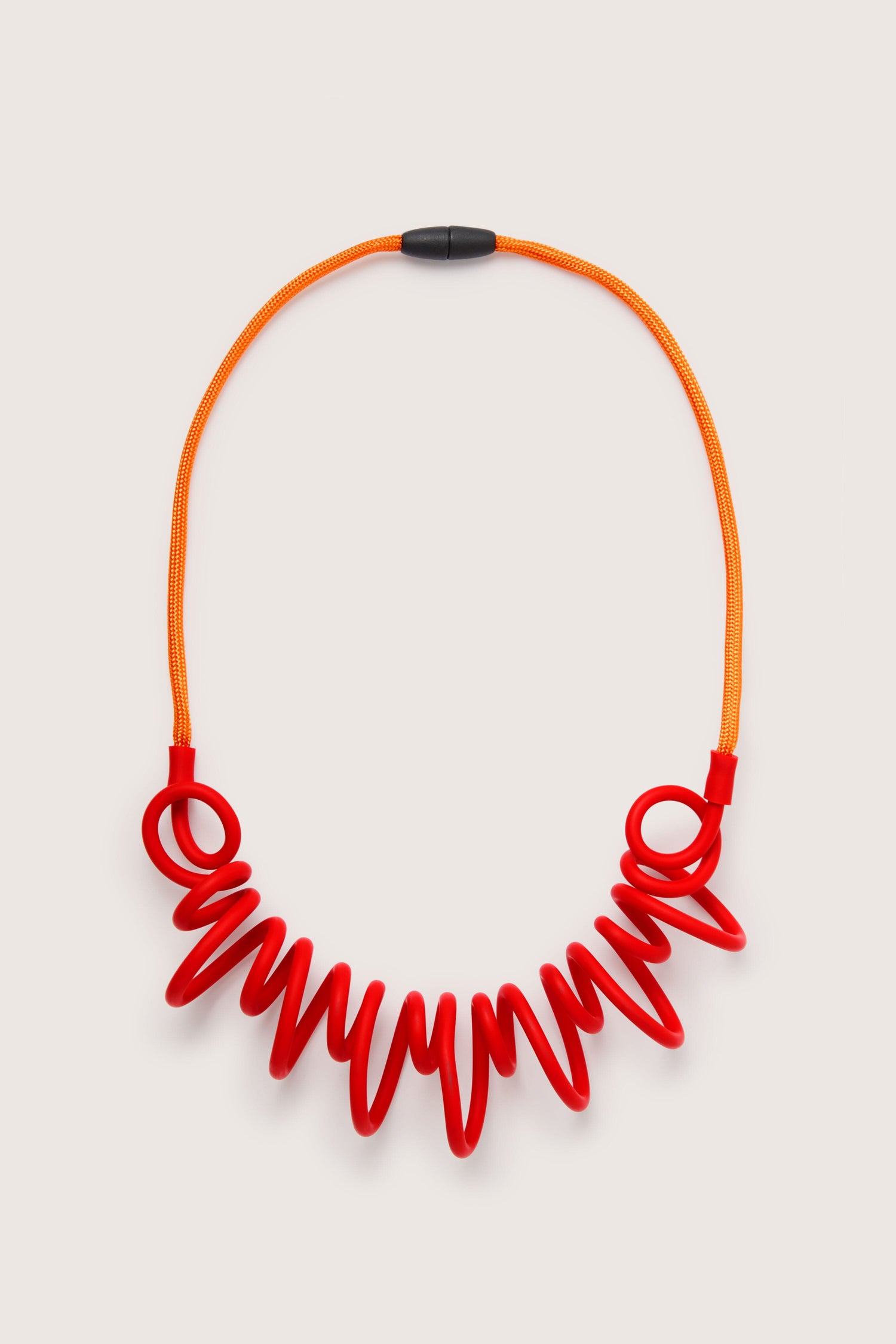 A contemporary jewellery piece, the Citrus Squiggle Necklace by Samuel Coraux, featuring a red and orange necklace on a white surface.