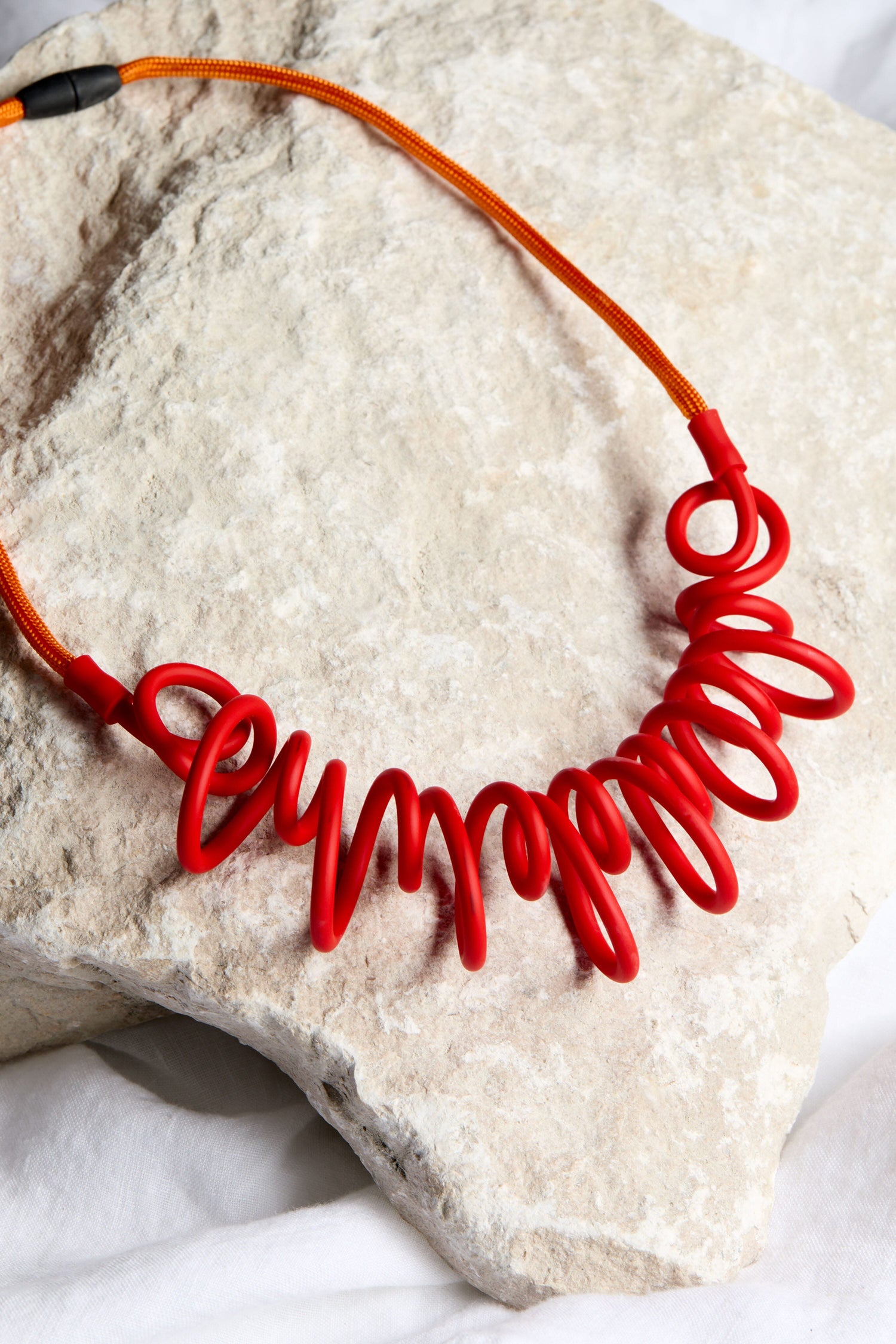 A contemporary Citrus Squiggle Necklace by Samuel Coraux showcased on a rock.