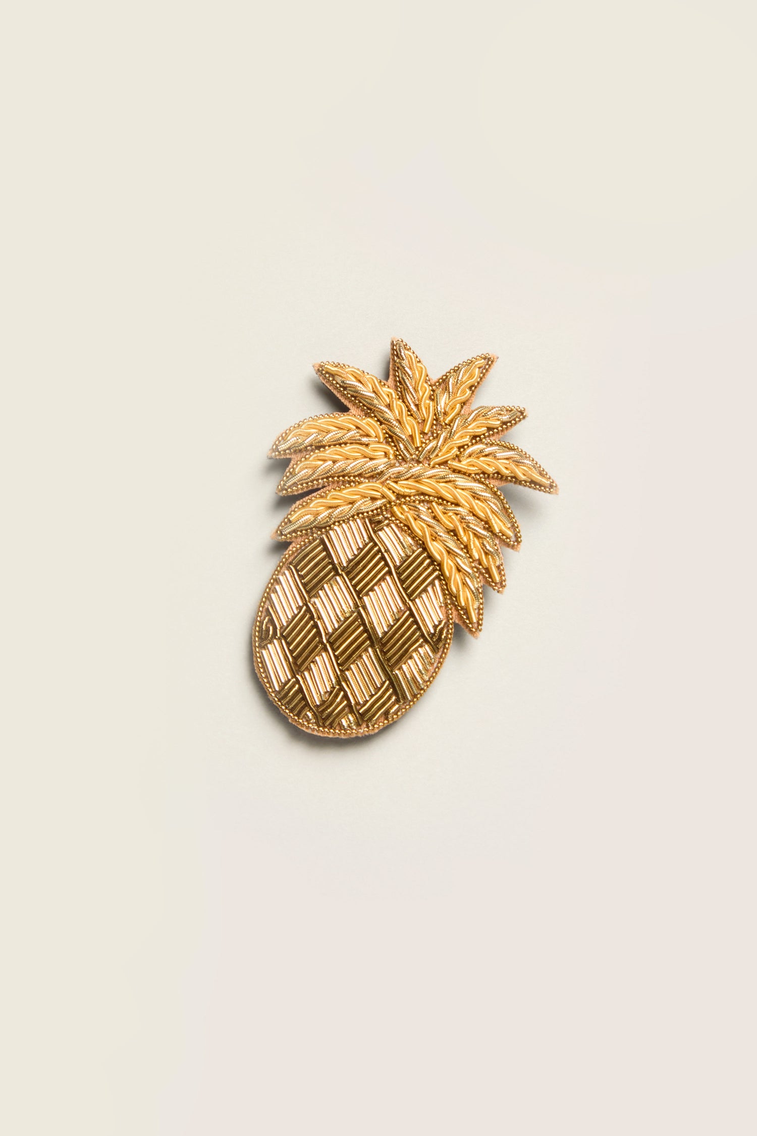 A Pineapple Brooch featuring textured gold details and adorned with golden beads sits against a plain background, adding a tropical twist.