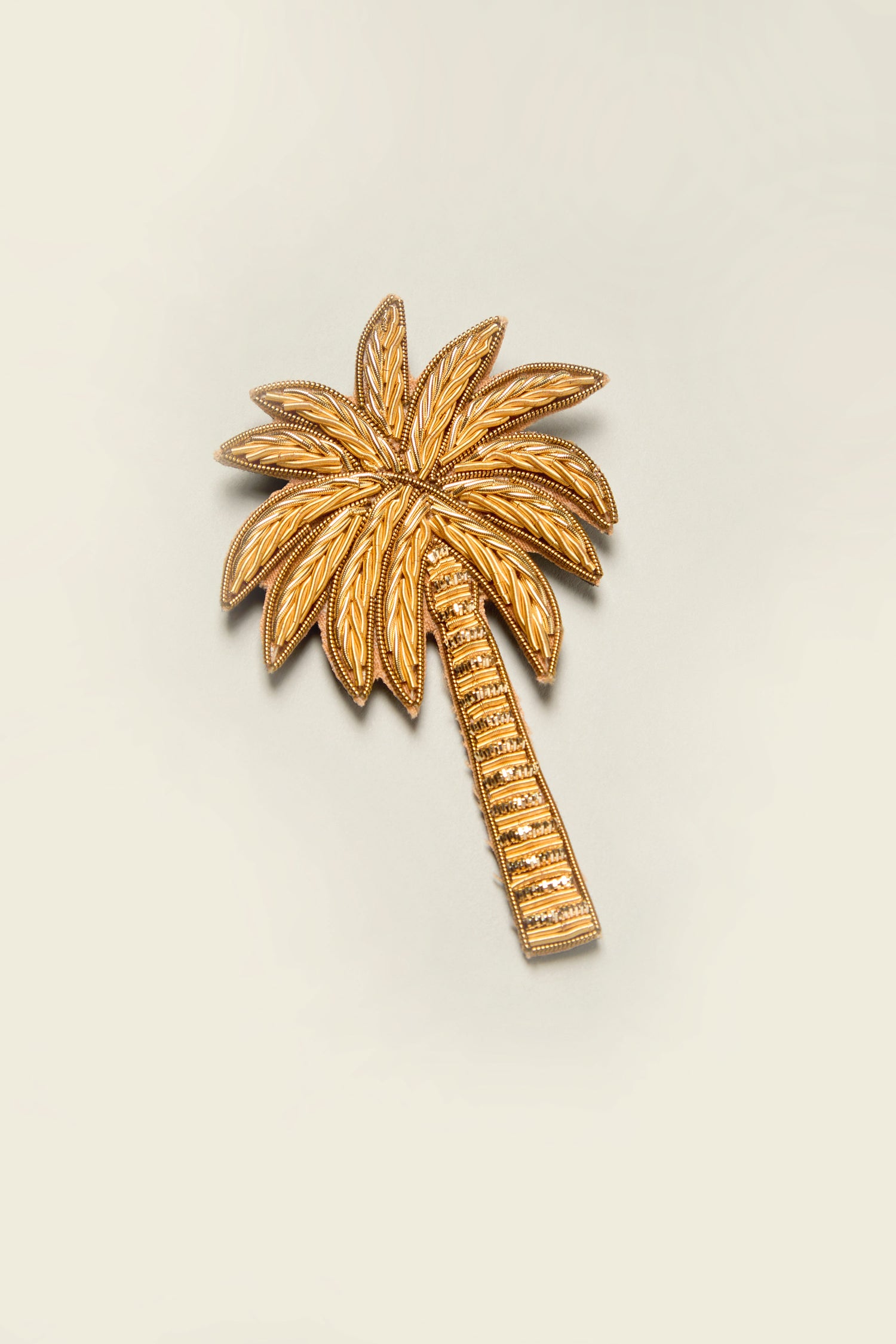 The Golden Palm Brooch, an elegant accessory embodying the shape of tropical palms, shines brilliantly in its radiant gold color against a light background.