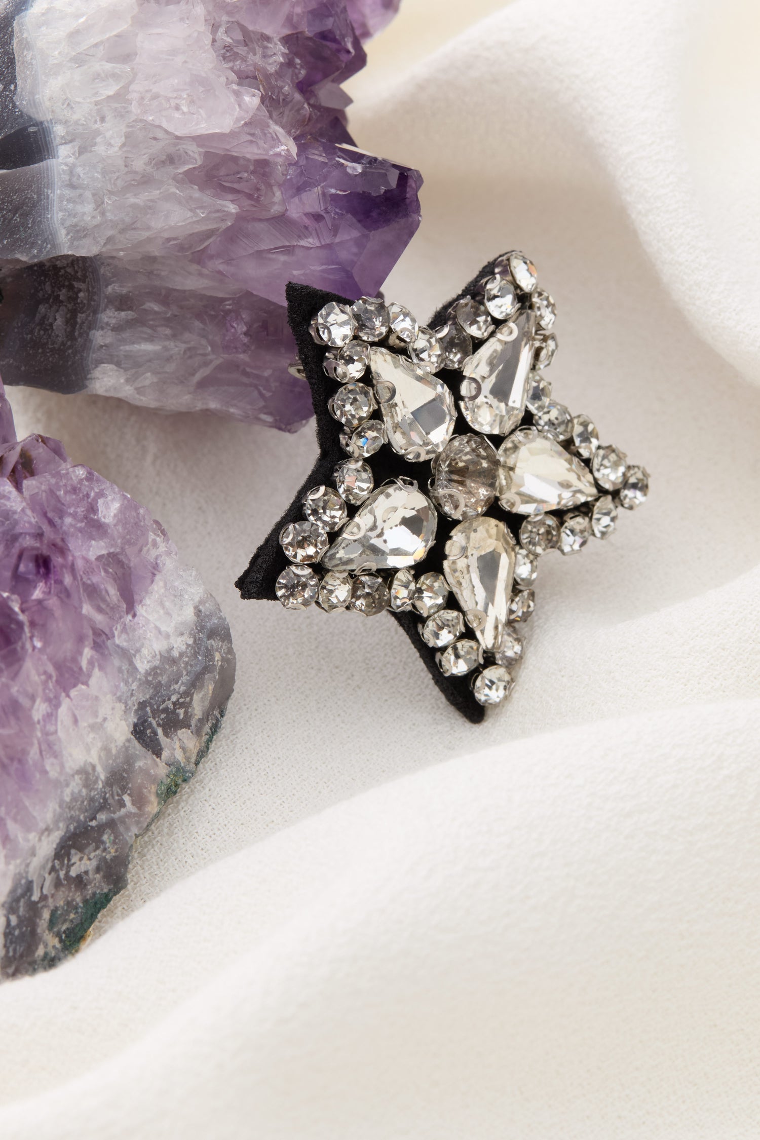 Star Brooch adorned with teardrop and circular rhinestones, displayed on white fabric beside amethyst geodes.