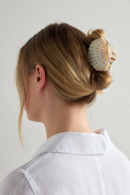 A person with blonde hair, styled in an updo, is wearing a white blouse and a Hand Painted Seashell Hair Clip while facing away from the camera.