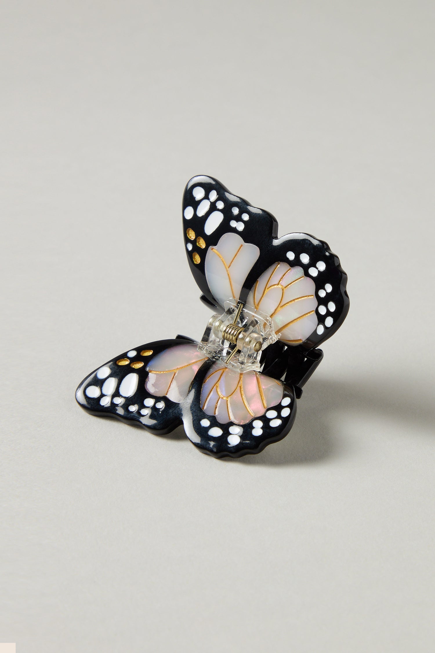 The Hand Painted Mini Monarch Hair Clip is butterfly-shaped and made from biodegradable acetate, featuring black, white, and pink details on a plain gray background.