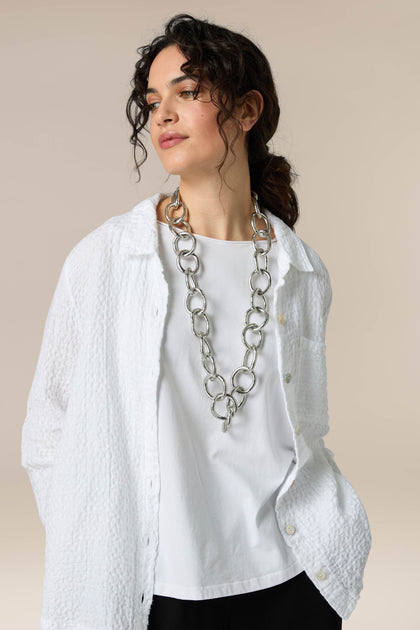 A woman, adorned with the Long Silver Links Necklace, is wearing a fresh sheen white shirt and black pants.