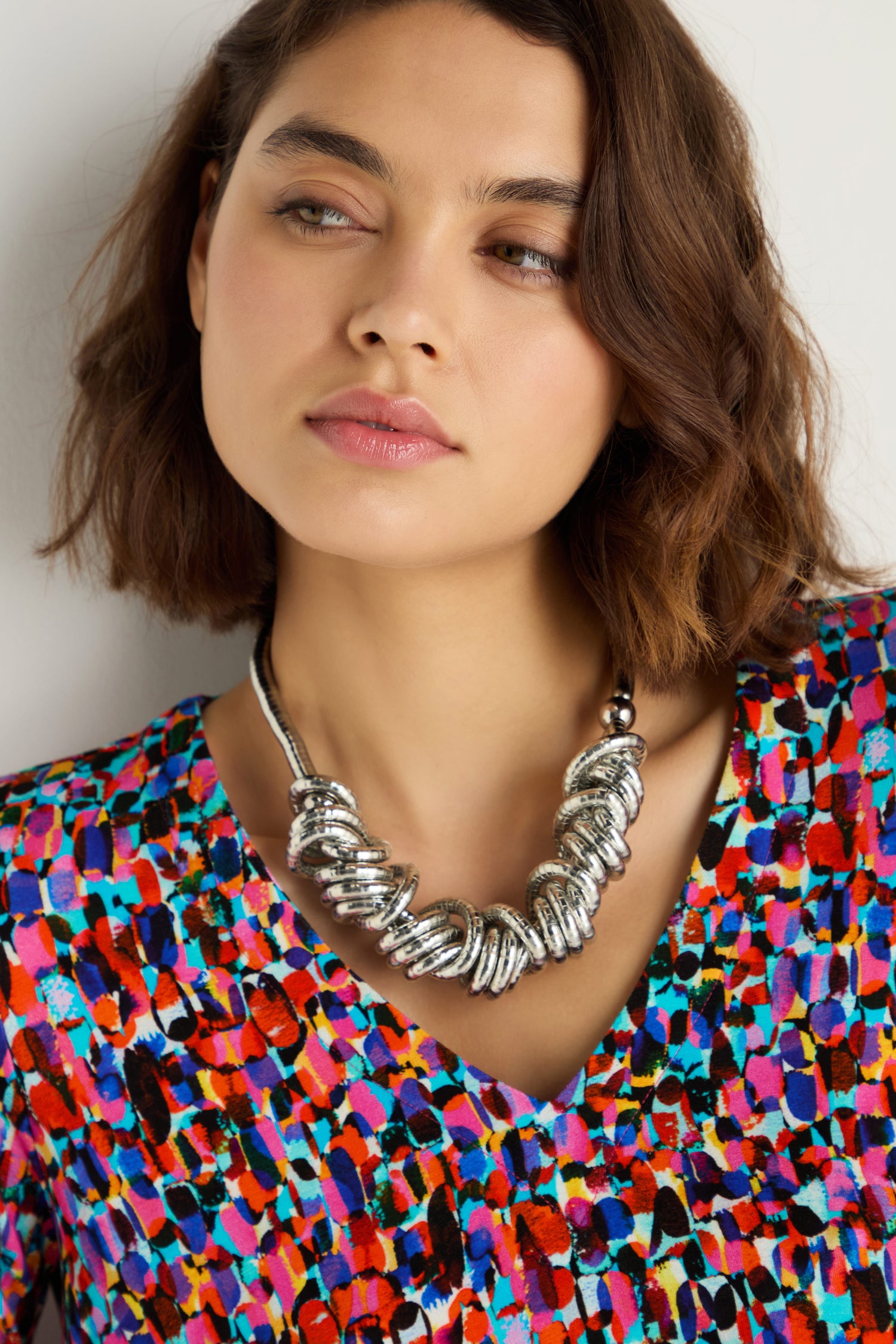 A woman with short brown hair wears a colorful patterned top and a Woven Silver Necklace, looking slightly to the side.