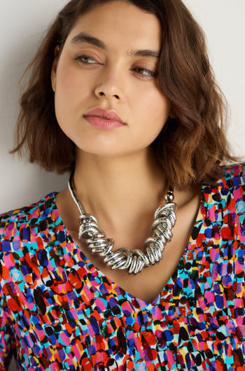 A woman with short brown hair wears a colorful patterned top and a Woven Silver Necklace, looking slightly to the side.