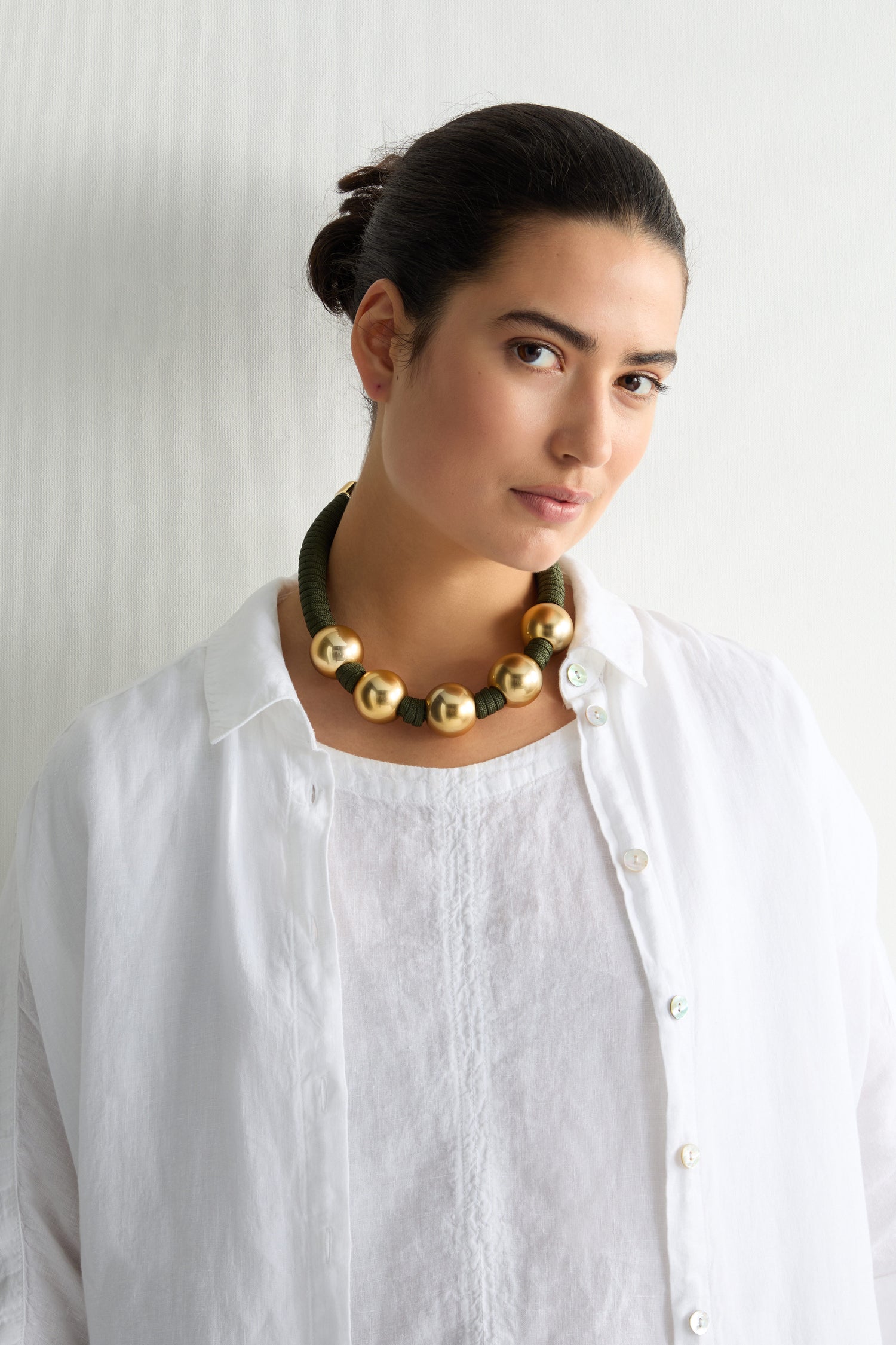 A person wearing a white shirt and a Gold Sphere Cord Necklace stands against a plain background.