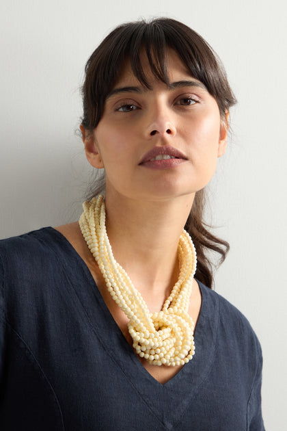 A long-haired individual in a dark shirt exudes artisanal charm against a plain background, wearing the versatile and elegant Knotted Bead Necklace.