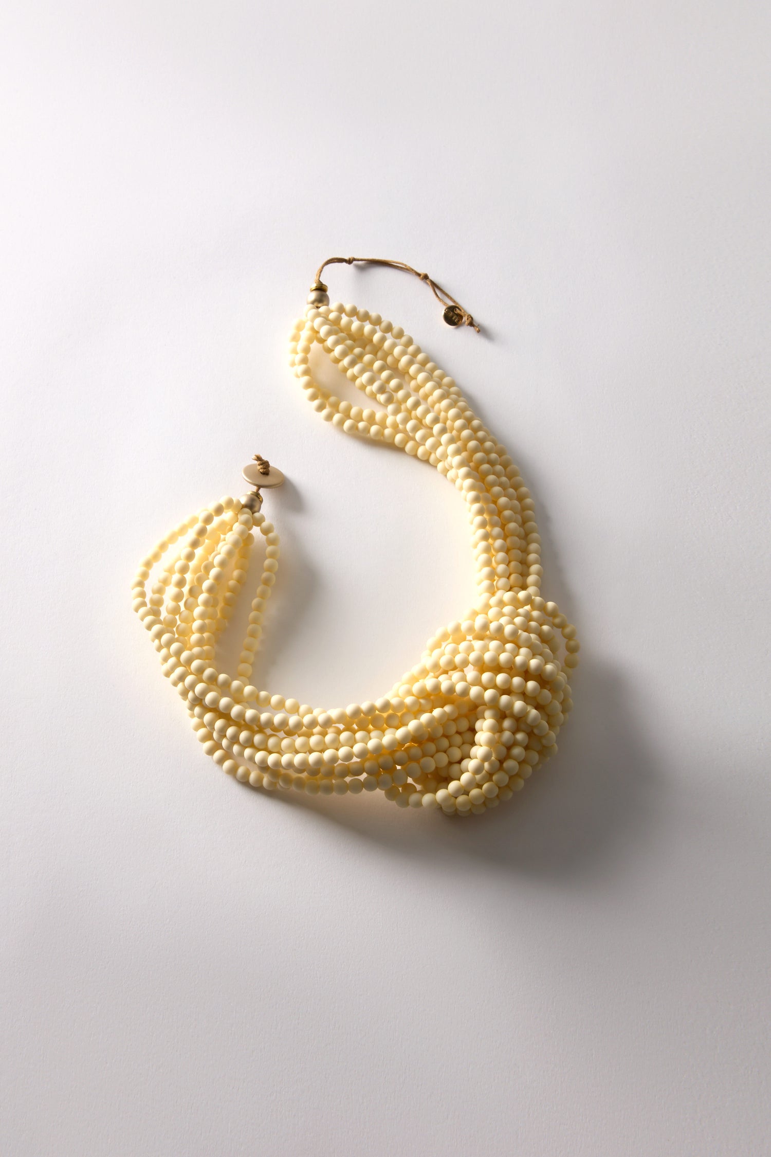 A Knotted Bead Necklace with multi-strand beads and a twisted design rests on a white surface, exuding artisanal charm.