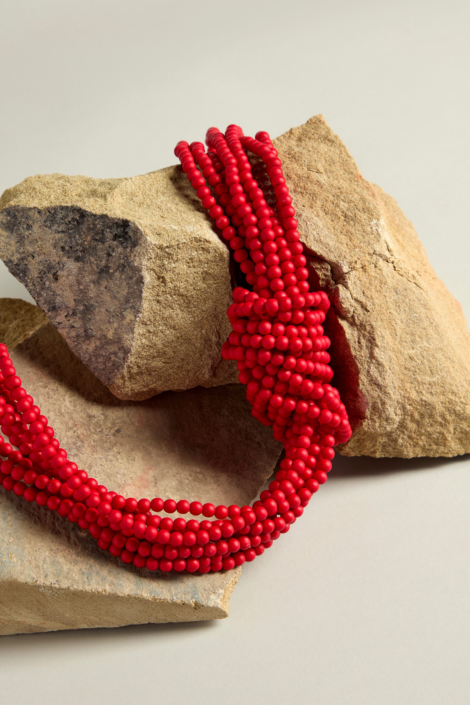 Knotted Bead Necklace draped over two beige and gray rocks on a neutral background, showcasing a statement piece with vibrant beads.