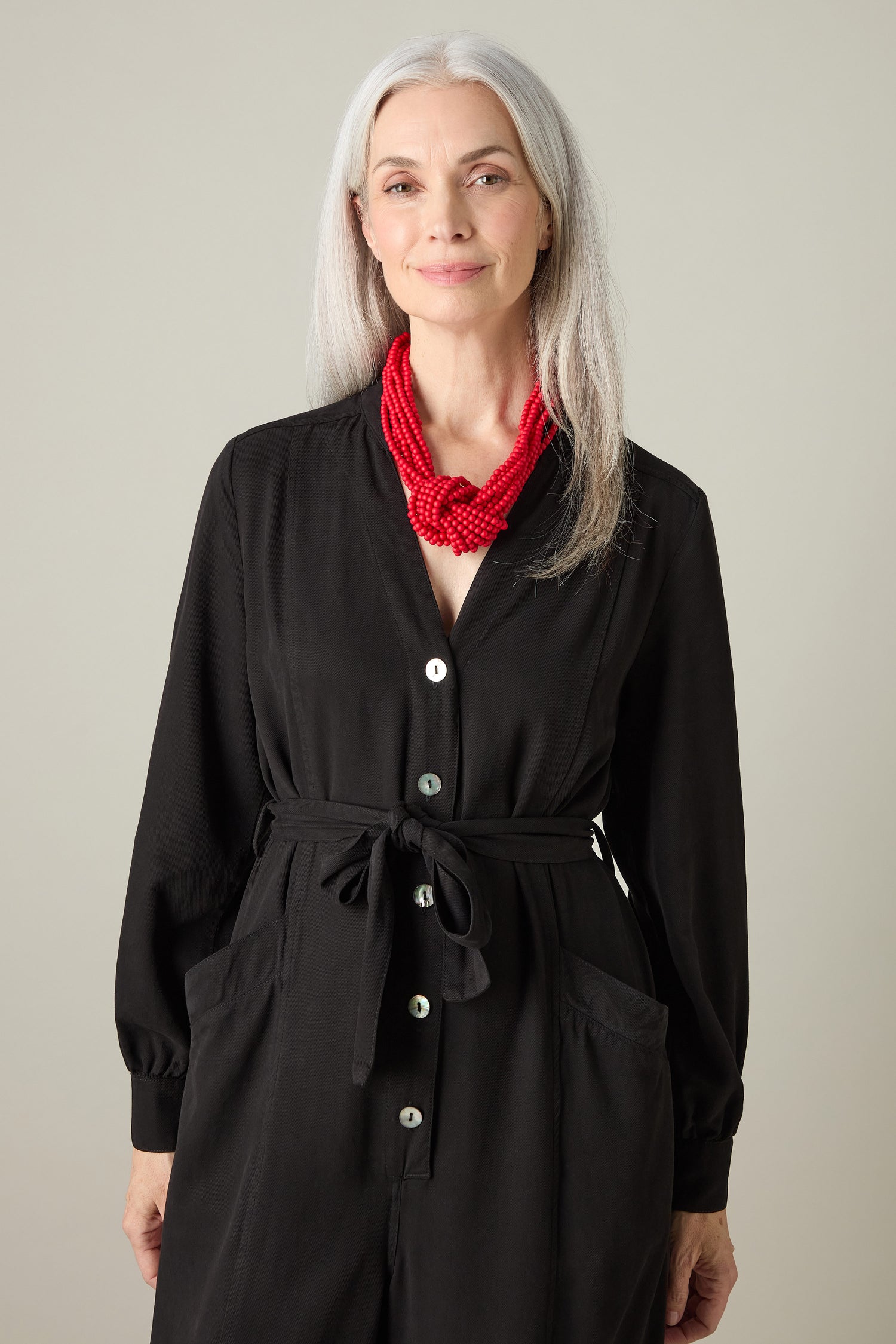 A woman with long gray hair models a black buttoned dress and makes a bold fashion statement with the vibrant Knotted Bead Necklace, standing against a plain background.