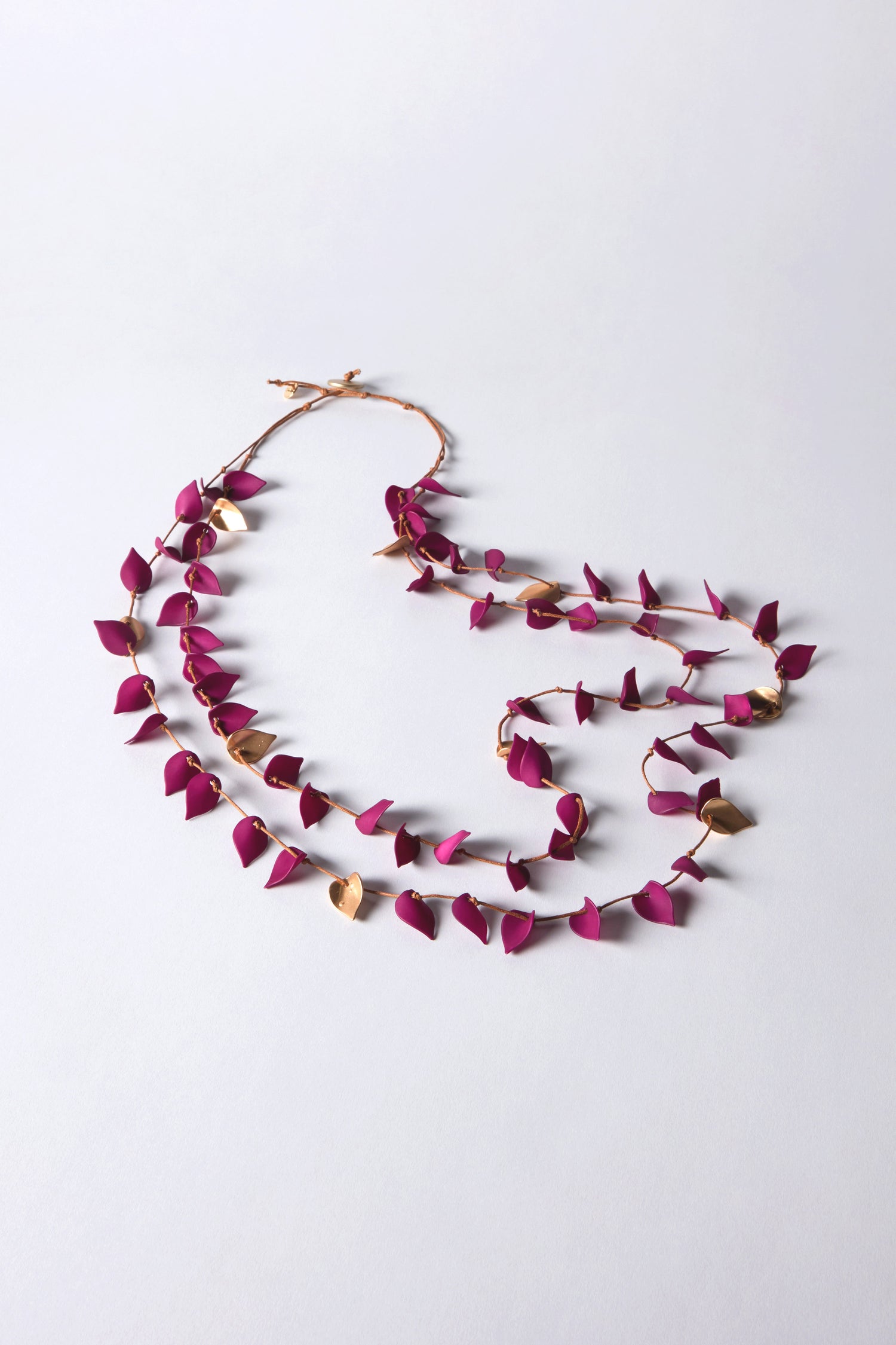 The Fuchsia Cascade Leaves Necklace features a gold chain with purple and gold-toned leaf-shaped elements, arranged beautifully in a flowing design against a light background.