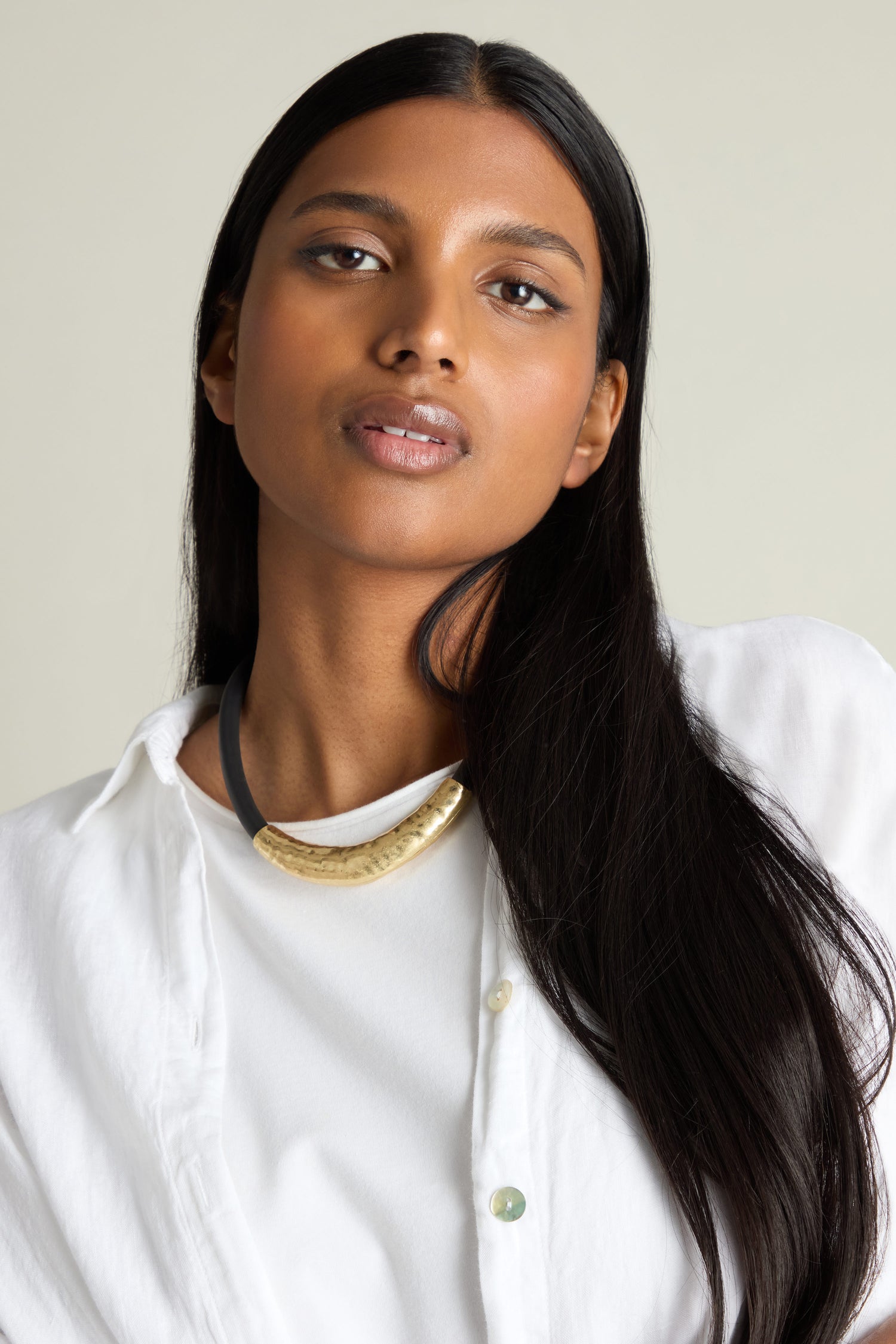 A person with long hair wears a white shirt and an eye-catching Hammered Necklace.