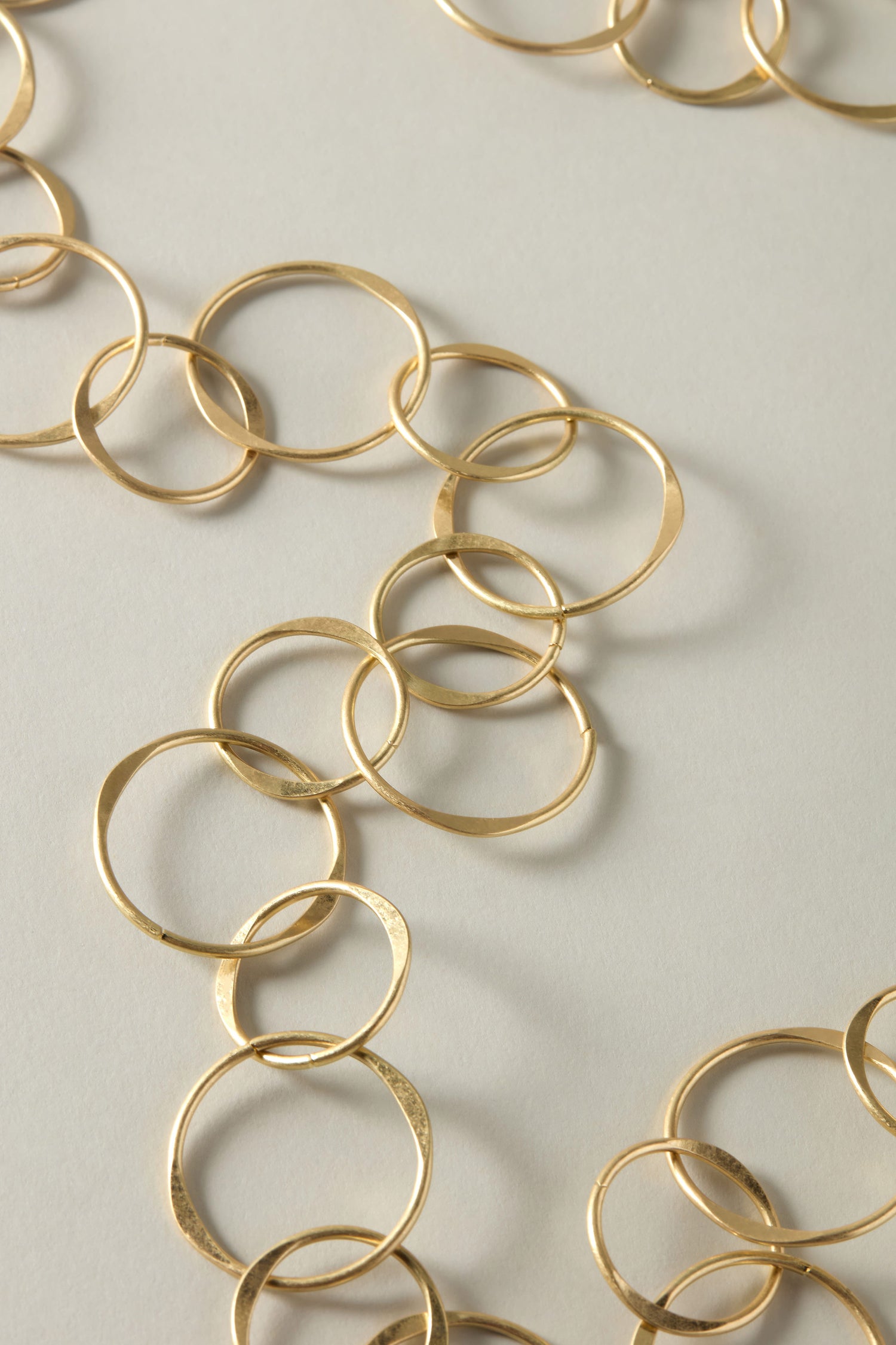 This close-up showcases the elegance of the Long Metal Hoop Necklace, featuring interlocking circular links meticulously arranged on a light gray surface.