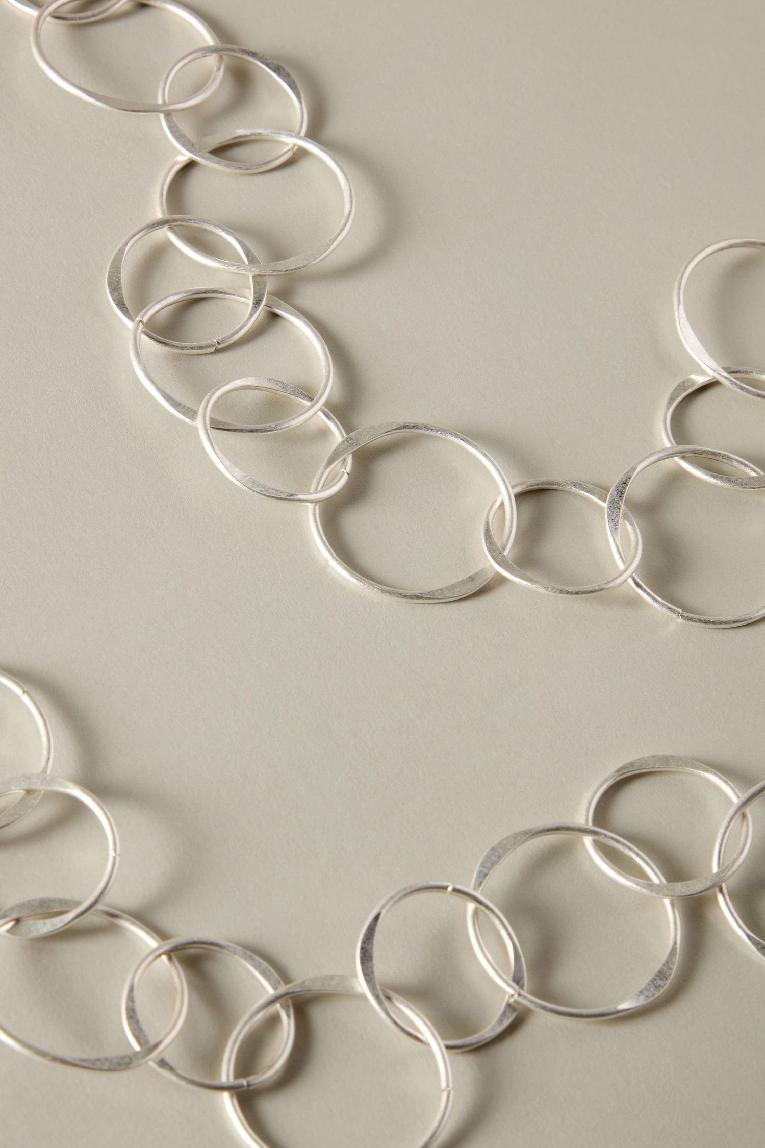 Close-up of a Long Metal Hoop Necklace with interlocking circular links, displayed on a light beige surface—this silver chain necklace truly captures the essence of bold jewelry as a statement piece.