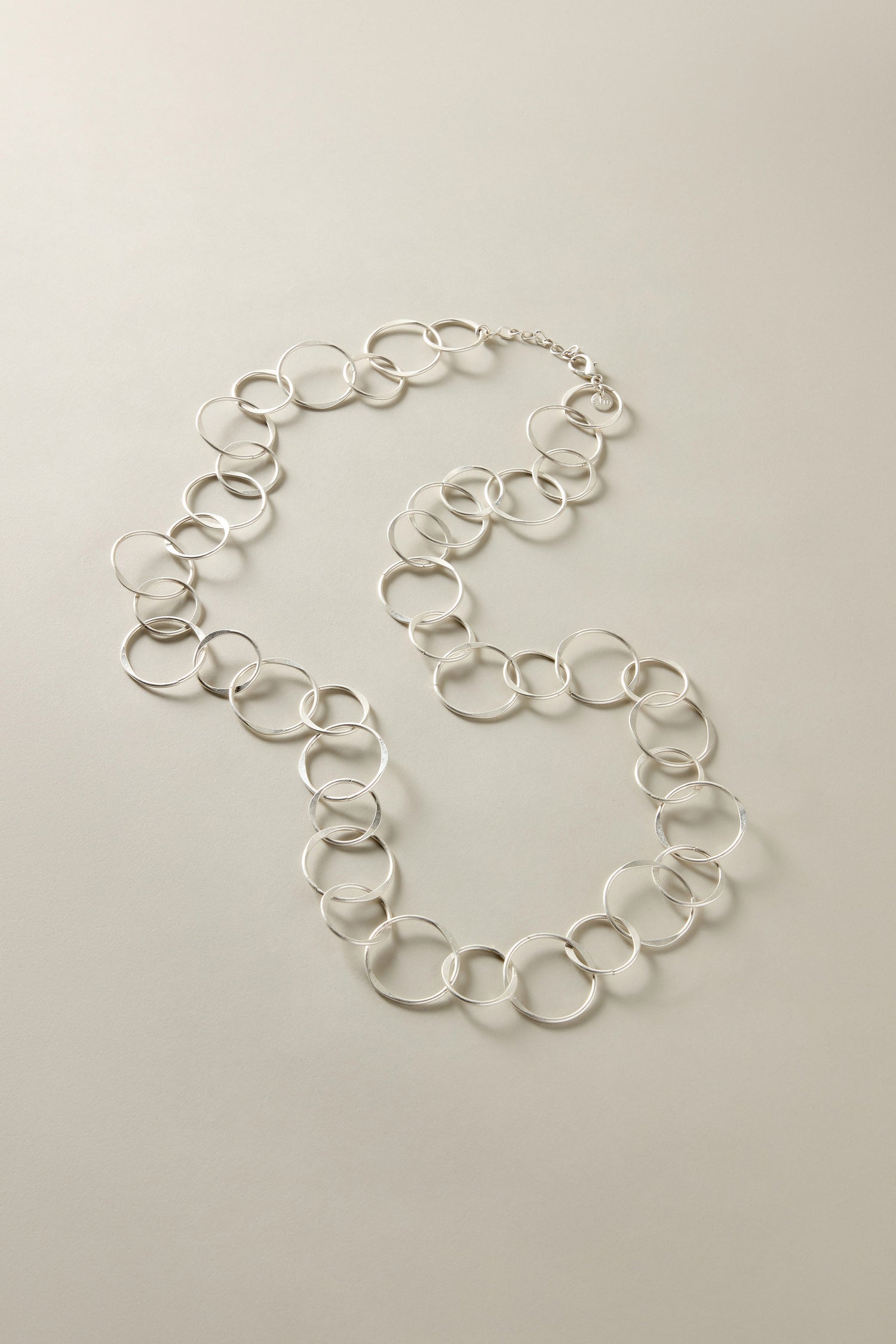 This Long Metal Hoop Necklace exemplifies bold jewelry with its silver design featuring large interlocking circle links against a light gray background, creating a striking statement piece.