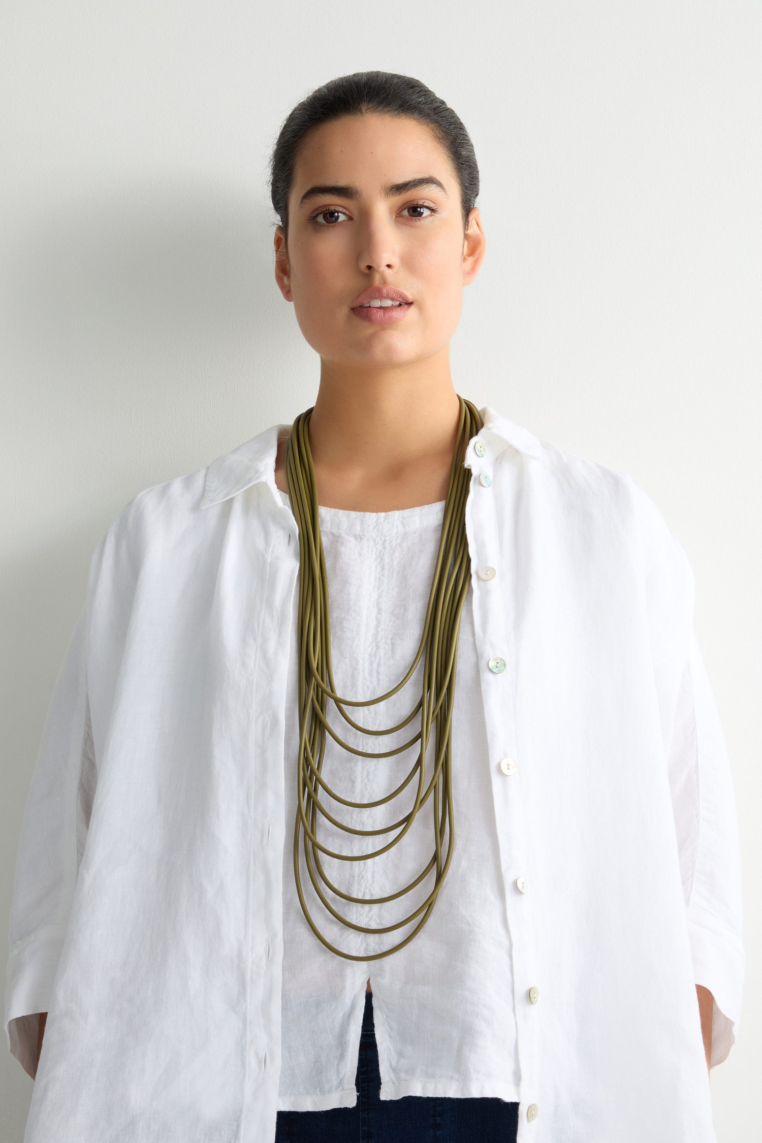 Against a plain background, someone wearing a white shirt showcases the Khaki Multi Strand Necklace featuring a discreet magnetic clasp.