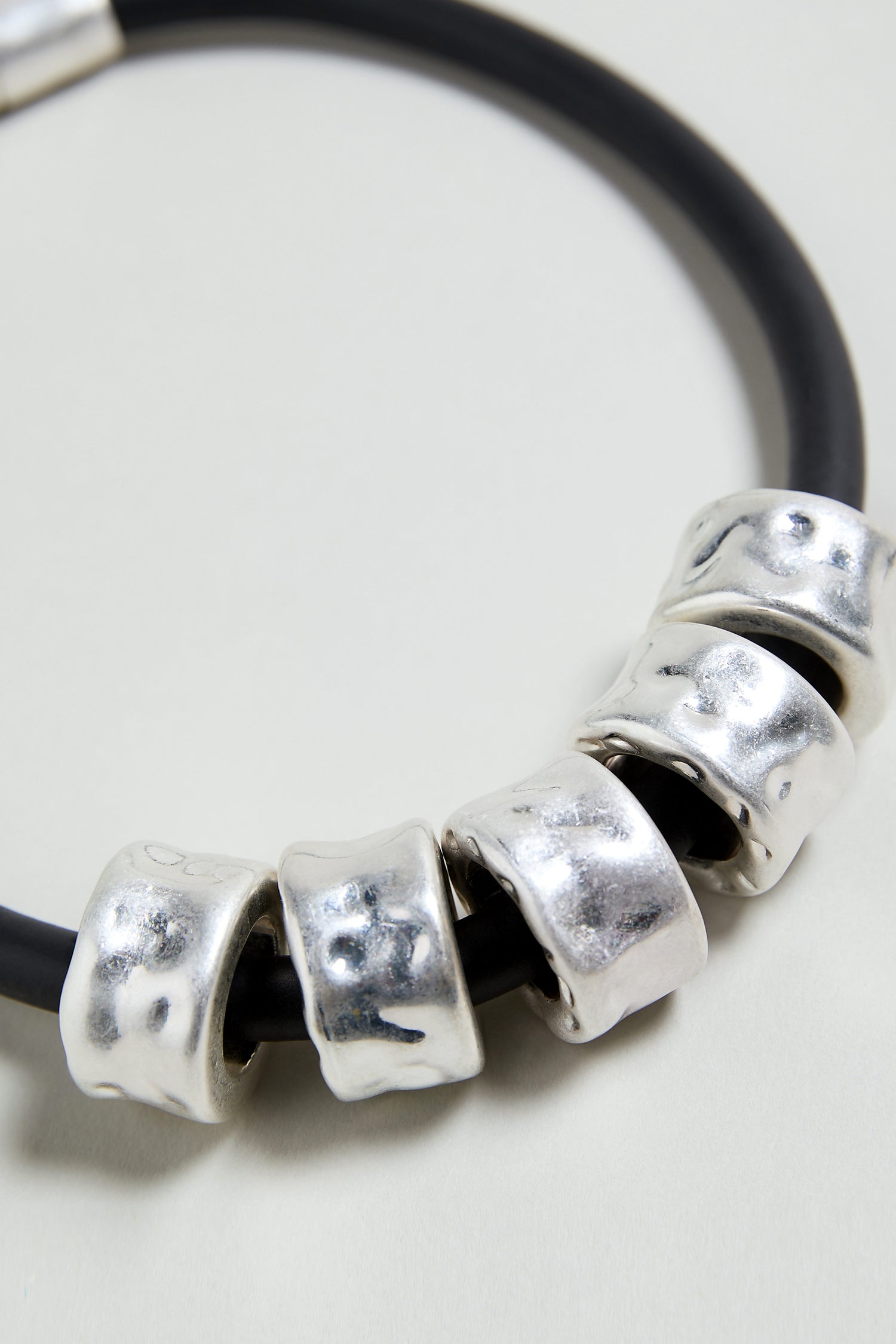The Hammered Cylinders Necklace is a black cord necklace with five closely arranged, irregular silver cylinder beads for a modern, sculptural look.