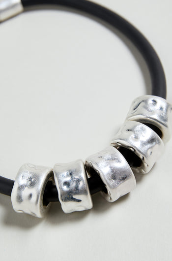 The Hammered Cylinders Necklace is a black cord necklace with five closely arranged, irregular silver cylinder beads for a modern, sculptural look.
