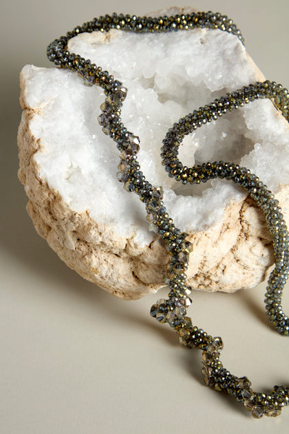 A Glacier Spiral Necklace, showcasing icy elegance, elegantly rests atop a textured rock adorned with a hollow, crystalline center on a simple surface.