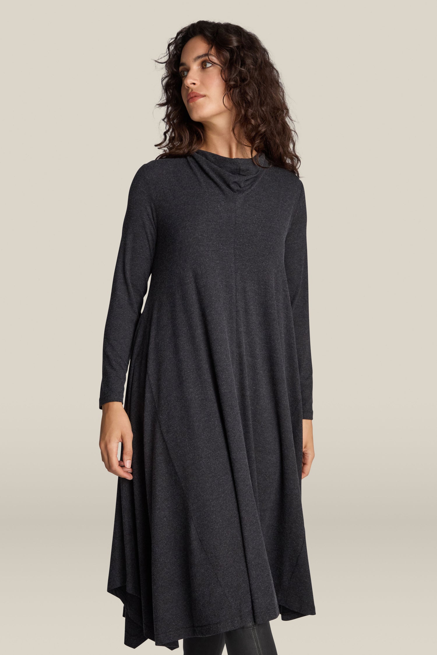 A person wearing the Soft Viscose Jersey Flared Dress in long-sleeved, dark grey with an asymmetrical design, looks to the side against a plain background.