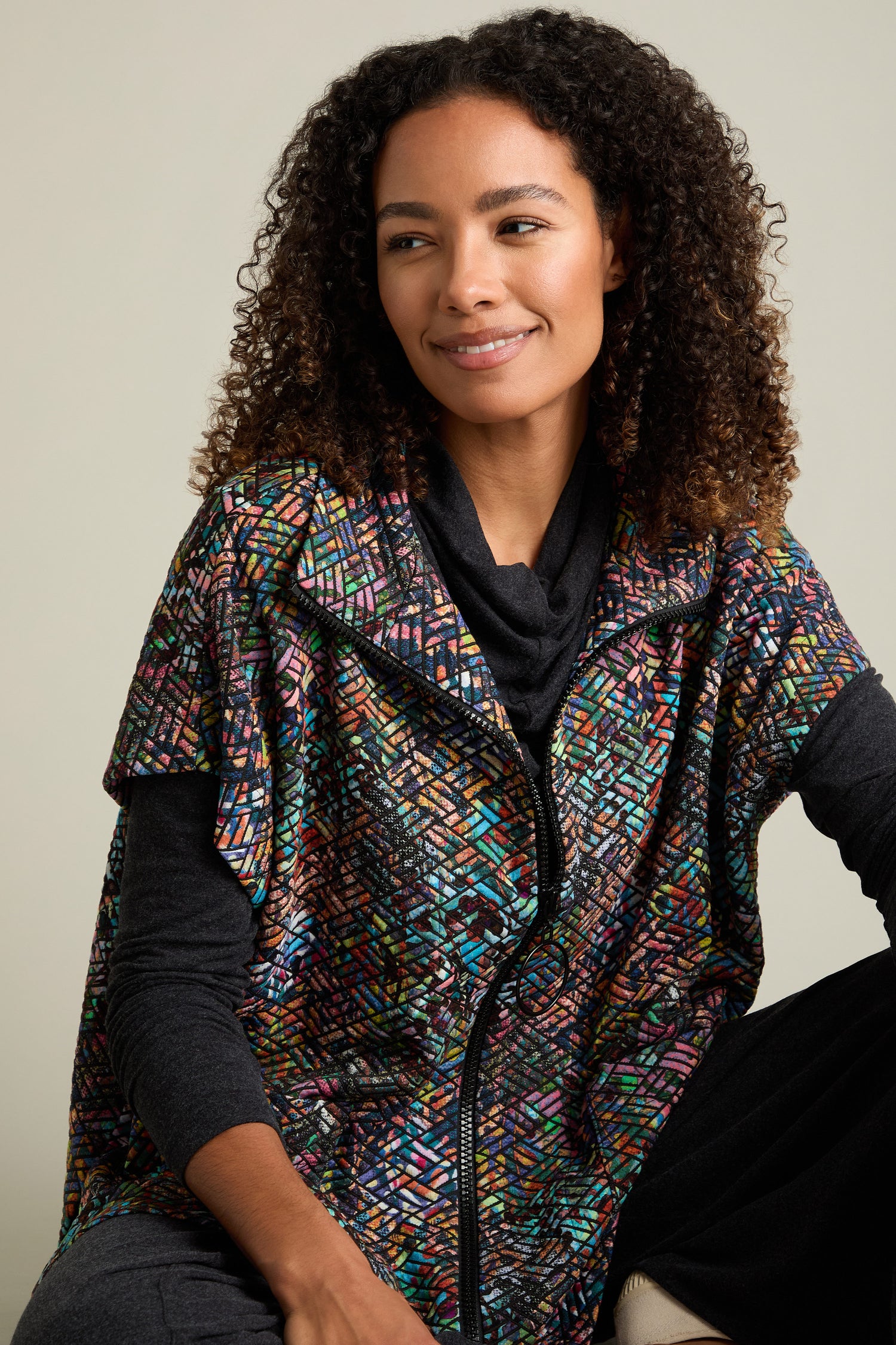 A person with curly hair smiles while wearing the vibrant Diamond Jacquard Jersey Jacket, featuring a colorful, patterned design crafted from multi-colored diamond jacquard fabric.