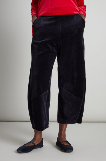 A person in a red long-sleeve shirt and black ballet flats, with hands in pockets, completes their look with the stylish and comfortable Velvet Jersey Bubble Trousers featuring an elasticated waist.