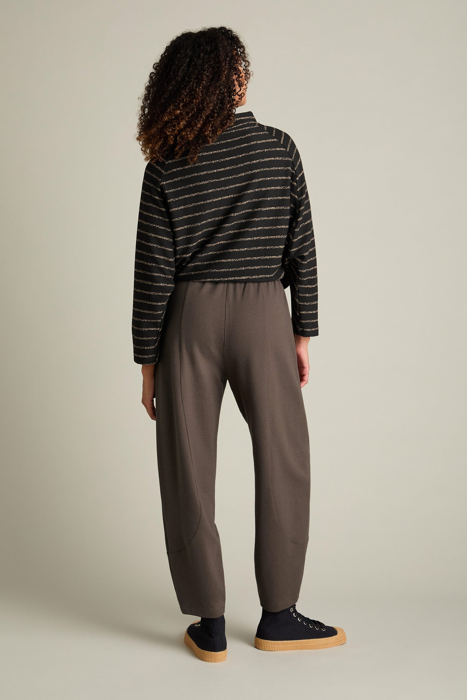 A person with curly hair is wearing a striped sweater and Marl Jersey Bubble Trousers, standing against a plain background. The ensemble captures a contemporary style, seamlessly blending comfort and flair.