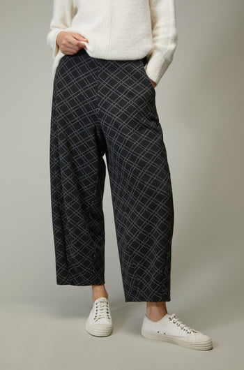 Person wearing Layered Square Jersey Jacquard Trouser featuring a modern grid pattern, paired with a white knit sweater and white sneakers, standing against a plain background.