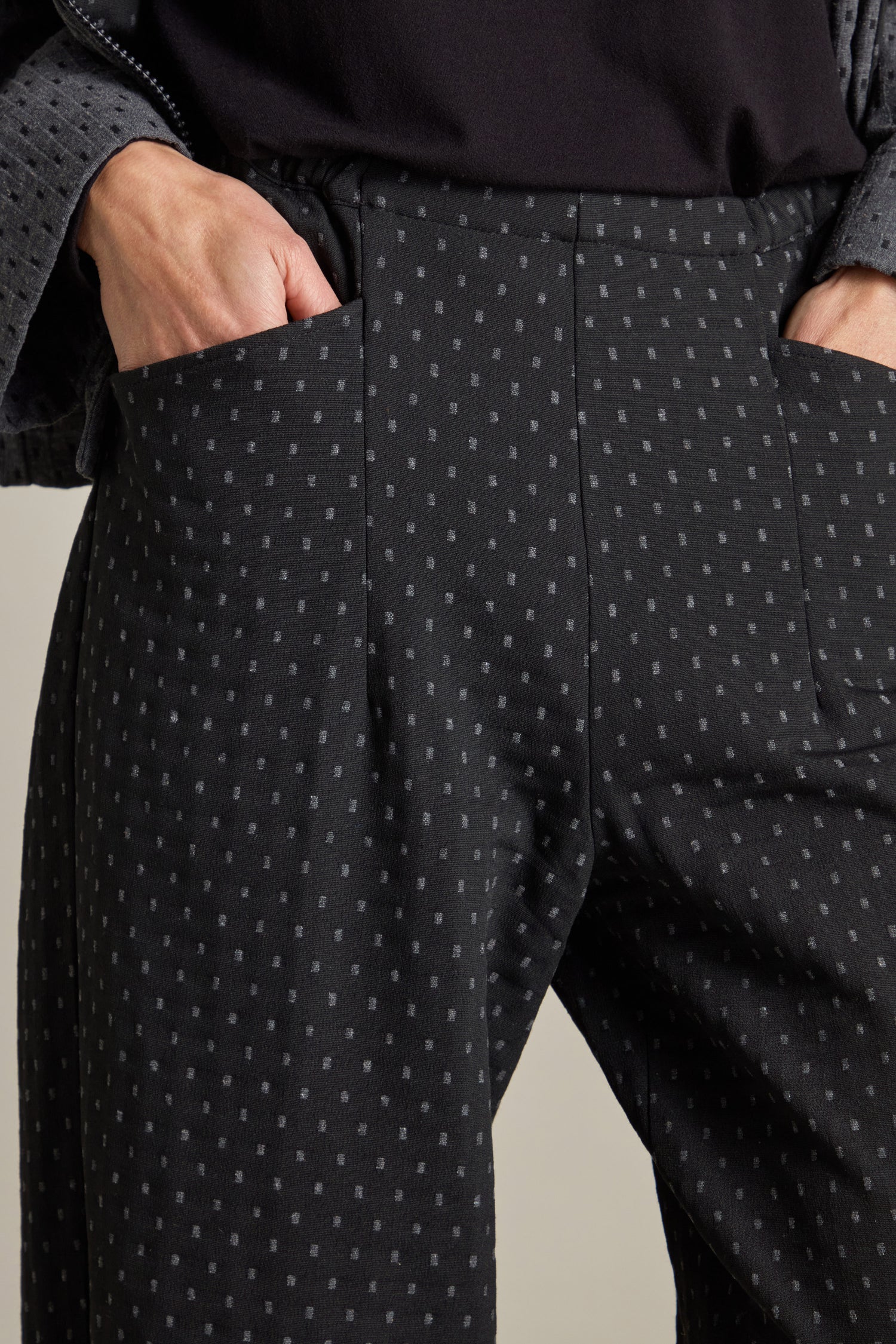 Close-up of a person wearing Square Jacquard Bubble Trouser featuring a dark, subtle dotted pattern and hands in pockets, paired with a matching double-faced jacquard fabric jacket.