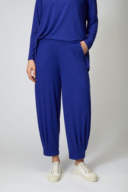 A person stands against a plain background wearing a loose, long-sleeved blue top and matching Soft Viscose Jersey Bubble Trouser with gathered ankles, paired with white sneakers.