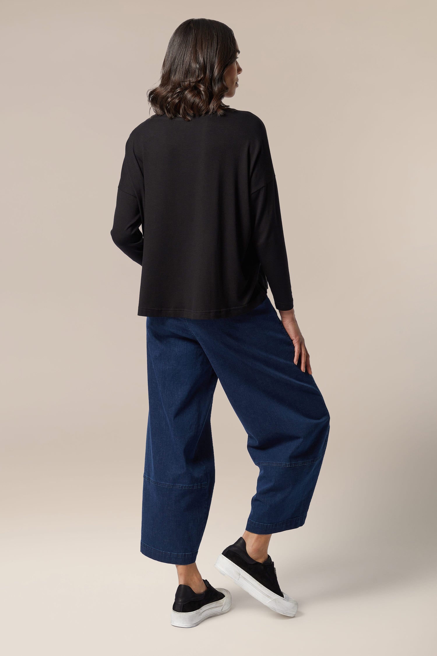 The back view of a woman wearing black pants and a Fluid Crepe Relaxed Top from her wardrobe.