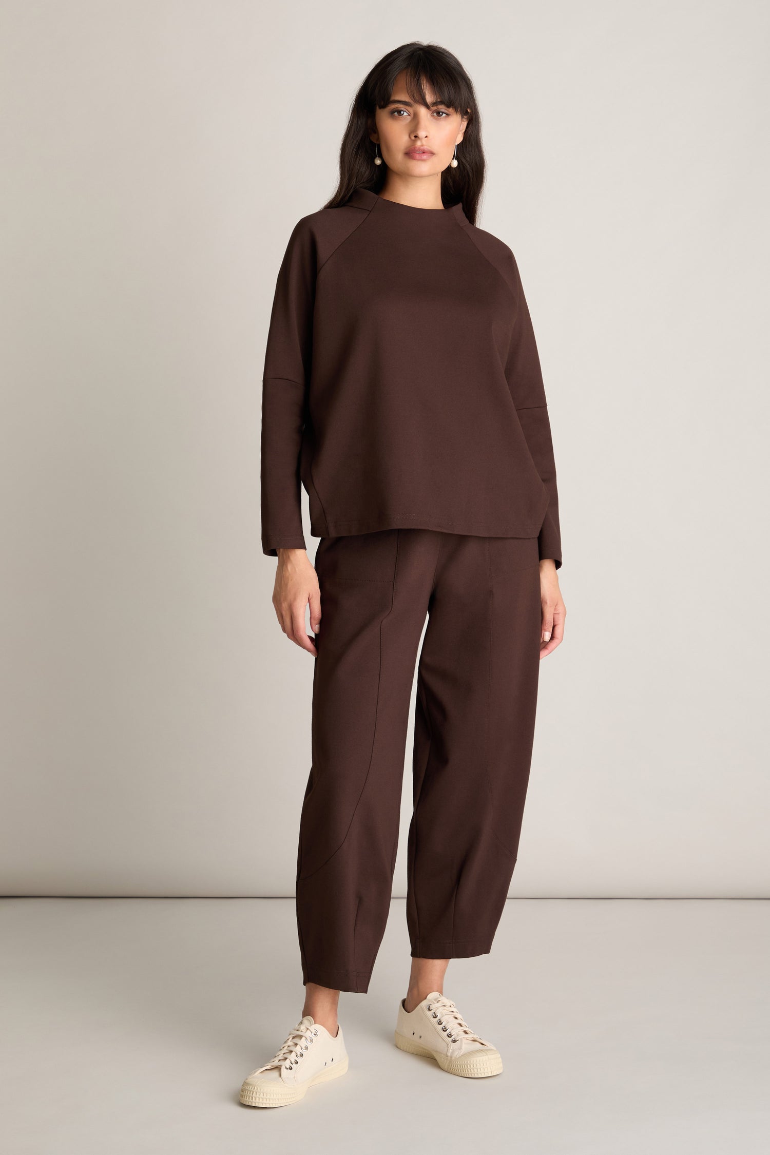 A person stands against a plain backdrop, sporting the Ponte Boxy Top along with matching brown trousers and beige sneakers for a casual chic look.