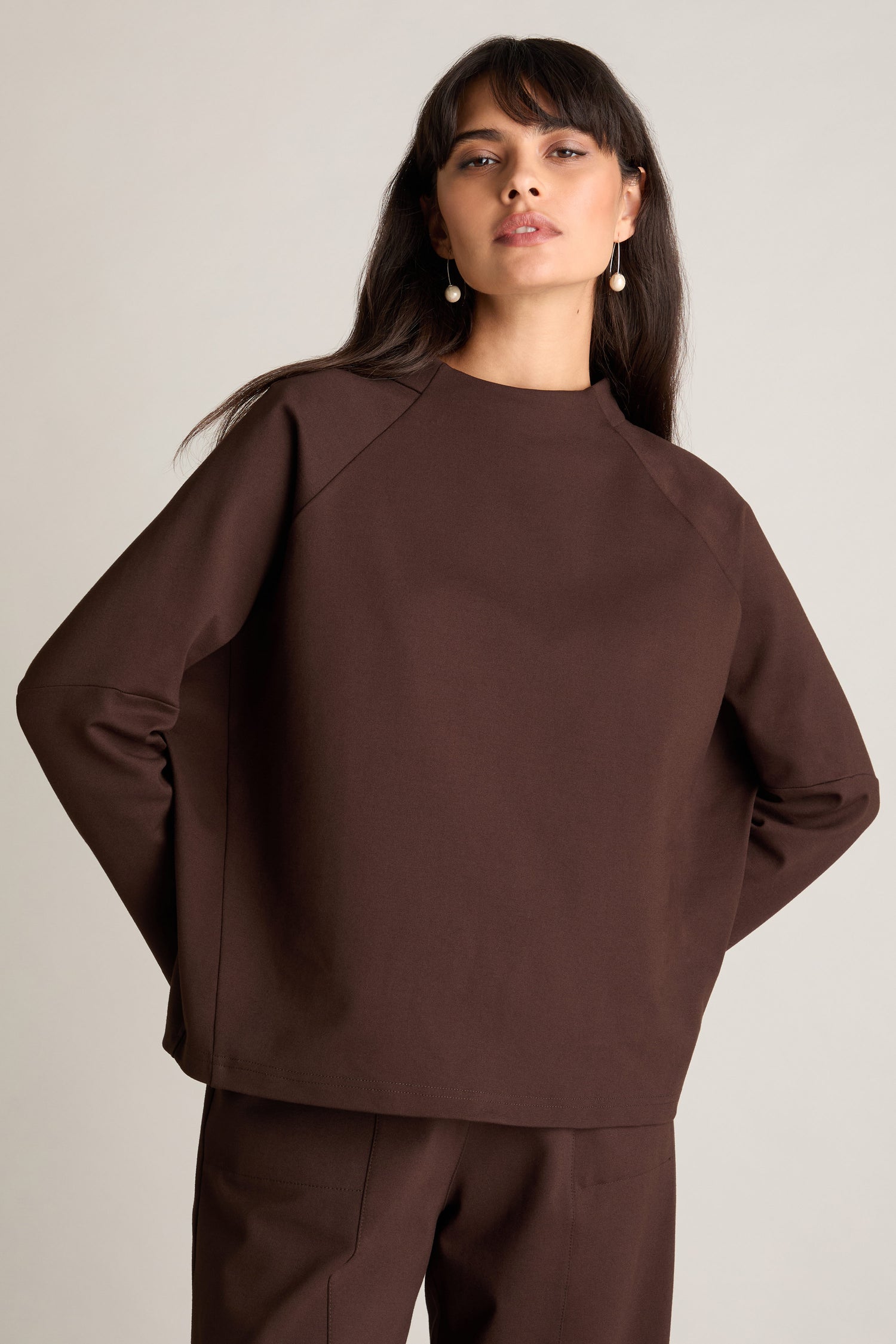 A woman in a brown Ponte Boxy Top, paired with matching pants, exudes a casual chic look as she stands against a plain background.