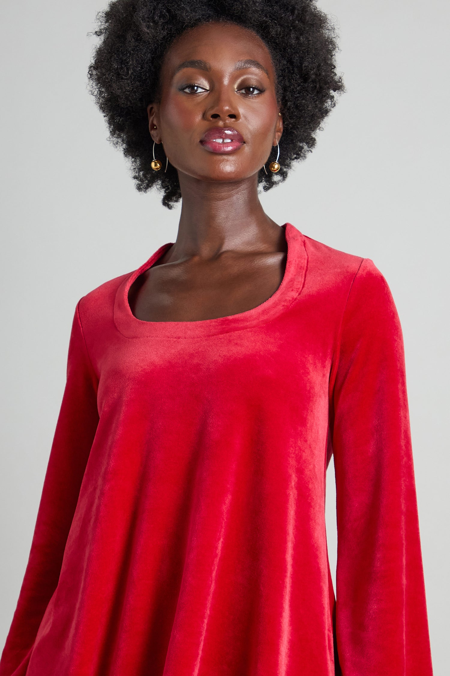 A person wearing the Velvet Jersey Horseshoe Neck Top in long-sleeve red velvet with a flattering fit-and-flare silhouette, looking forward.