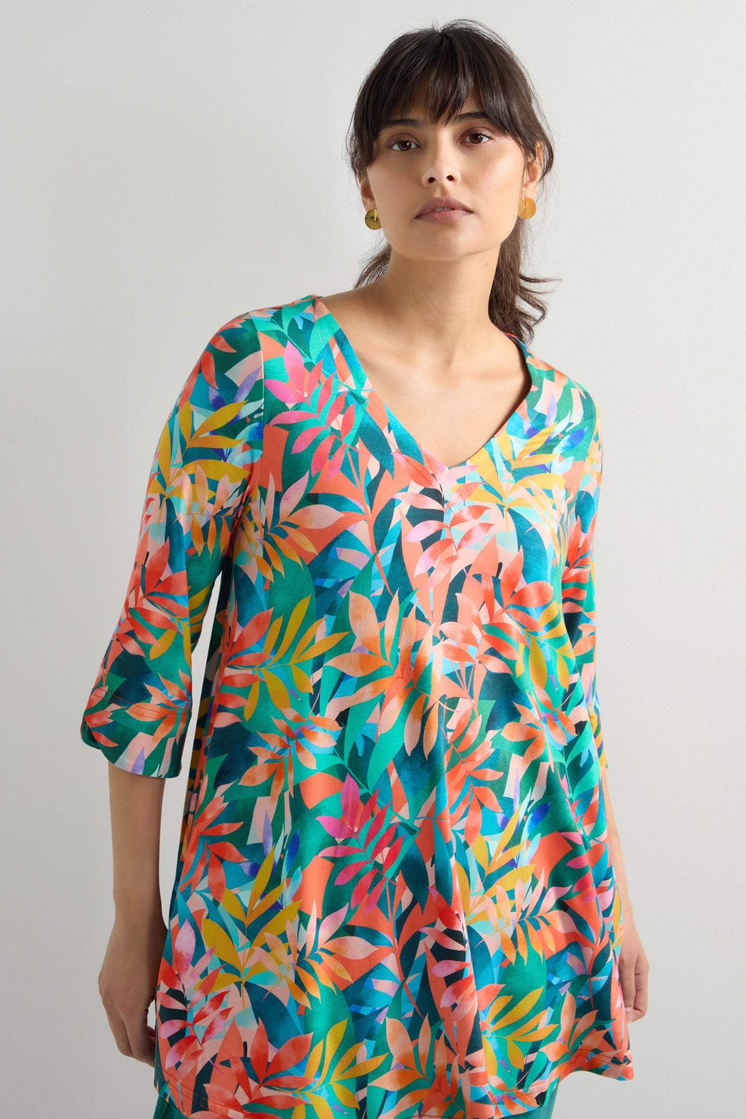 A person models a Tropical Leaves Jersey Print Tunic with a V-neck and elbow-length sleeves, standing gracefully against a neutral background to highlight its flattering fit.