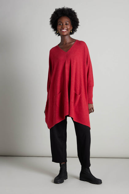 A person is wearing a red oversized V Neck Knit, ideal for layering in the cooler months, and has paired it with black pants and boots while standing against a plain background.