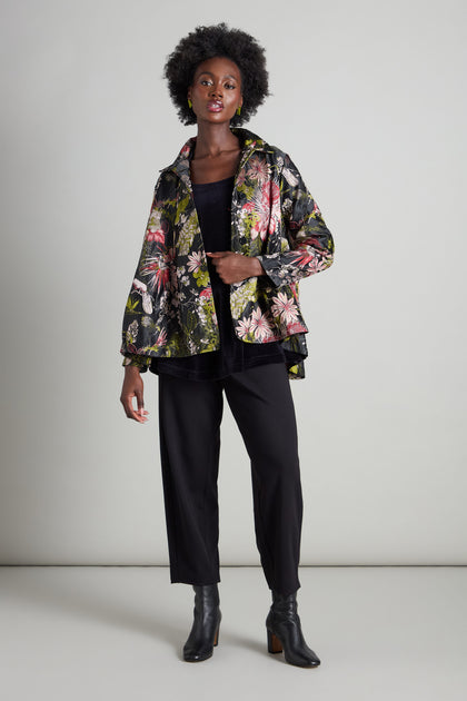 Dressed in a Jacquard Floral Jacket that evokes the charm of an Oriental garden, a person poses against a light gray backdrop wearing all black. This classic garment enhances their look with an air of sophistication.