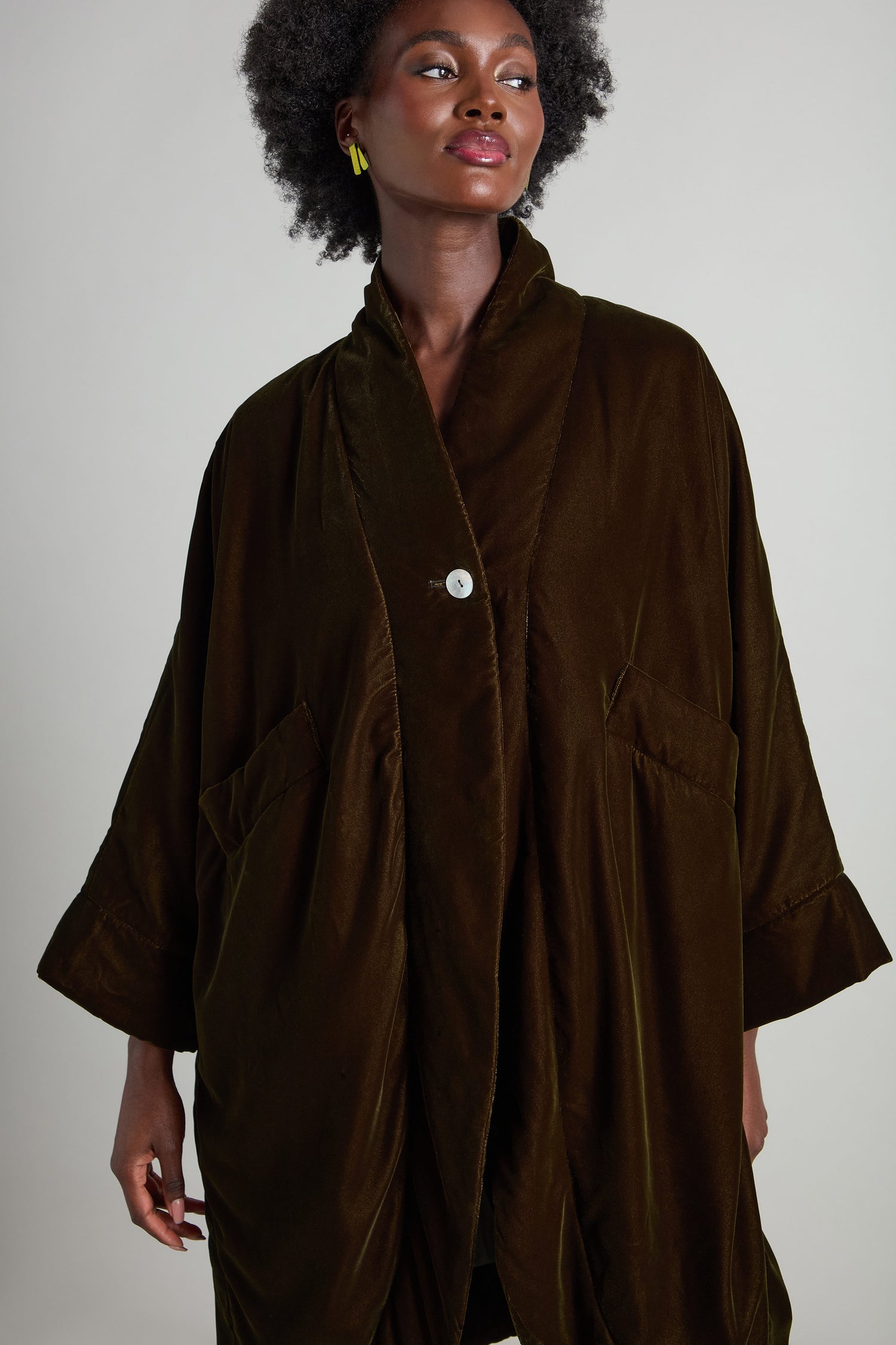 Against a plain backdrop, a person is adorned in the One Button Padded Velvet Coat, showcasing its luxurious oversized brown velvet design with two spacious pockets.