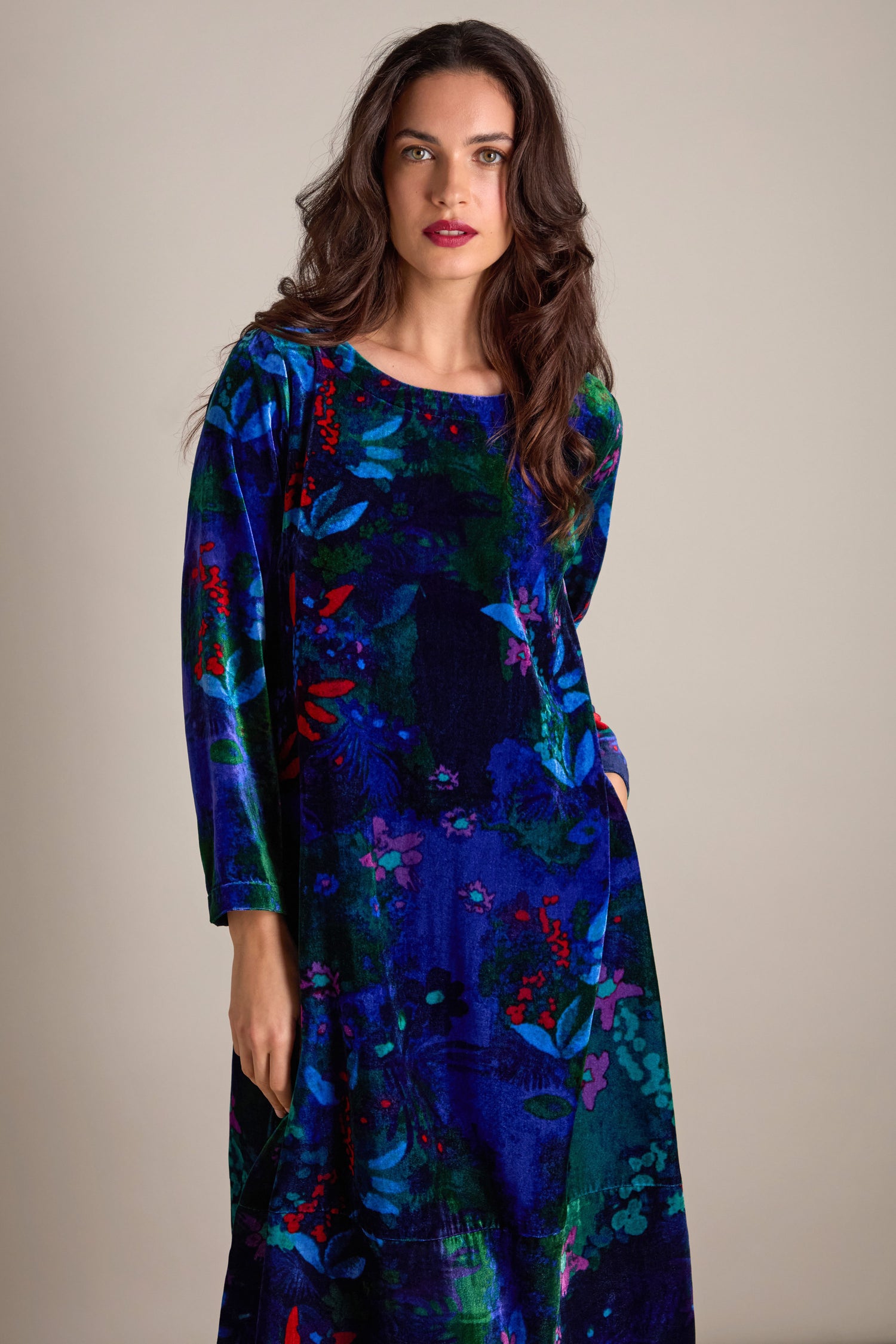 A person wearing the Late Night Flora Velvet Bubble Dress, featuring long sleeves and a vibrant blue floral pattern on velvet, stands against a plain background, making it perfect for evening events.