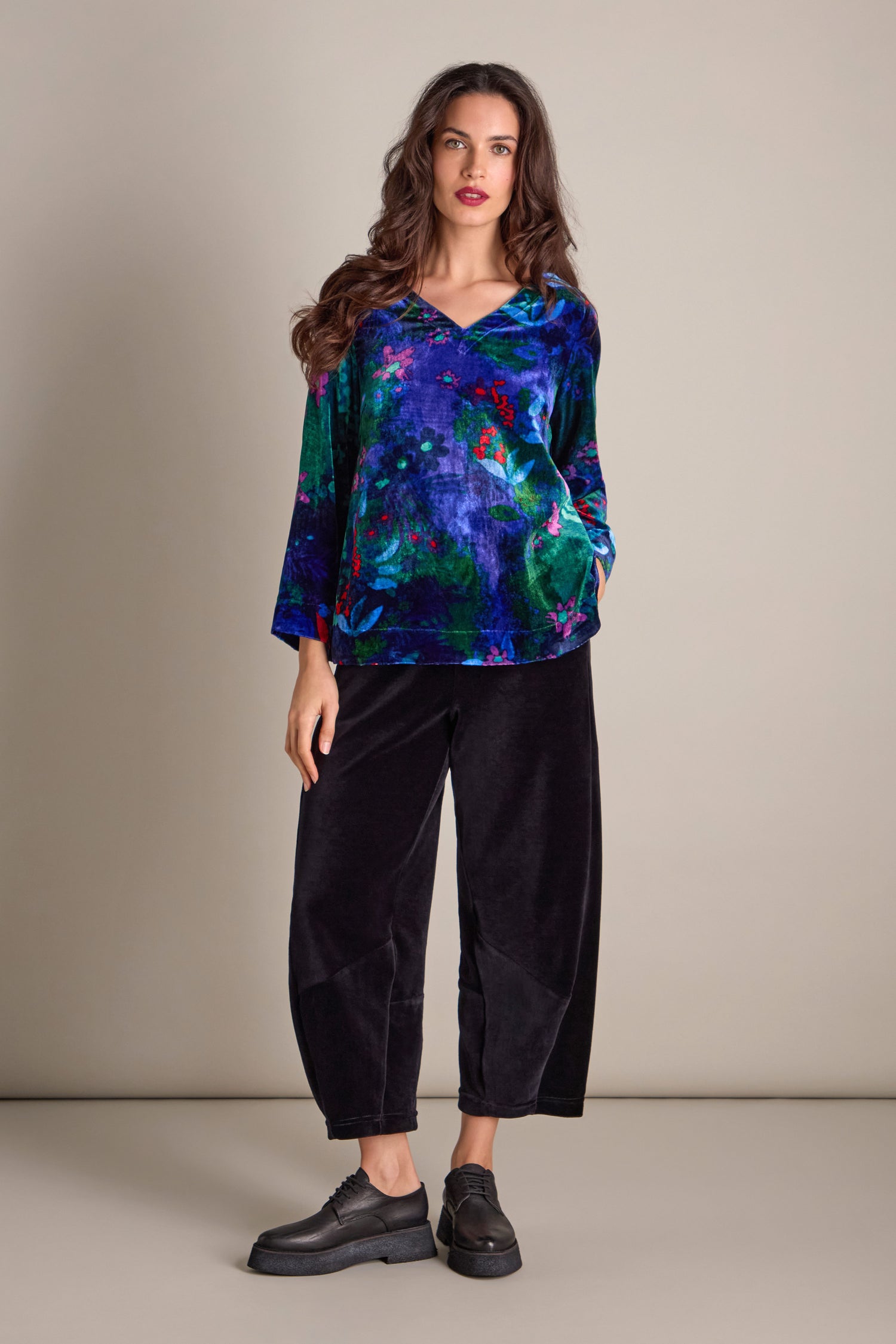 A woman dressed in the Late Night Flora Velvet Top paired with black pants poses against a simple backdrop, with the top's understated floral design contributing a hint of sophistication.