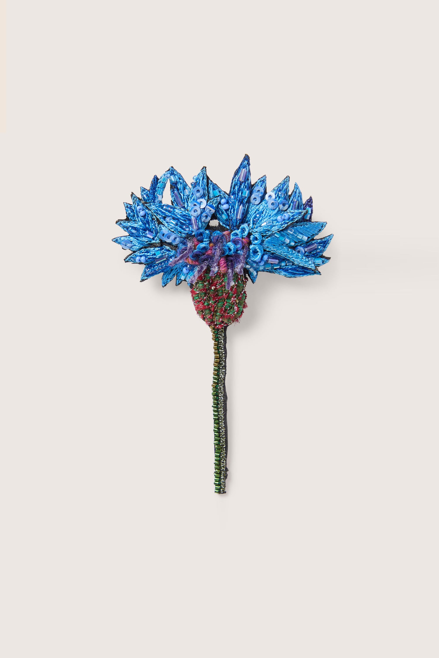 The Hand Embroidered Blue Cornflower Brooch features blue petals, a red center, and a green stem on a plain white background. Shimmering blue sequins enhance the elegance of this intricately designed accessory.